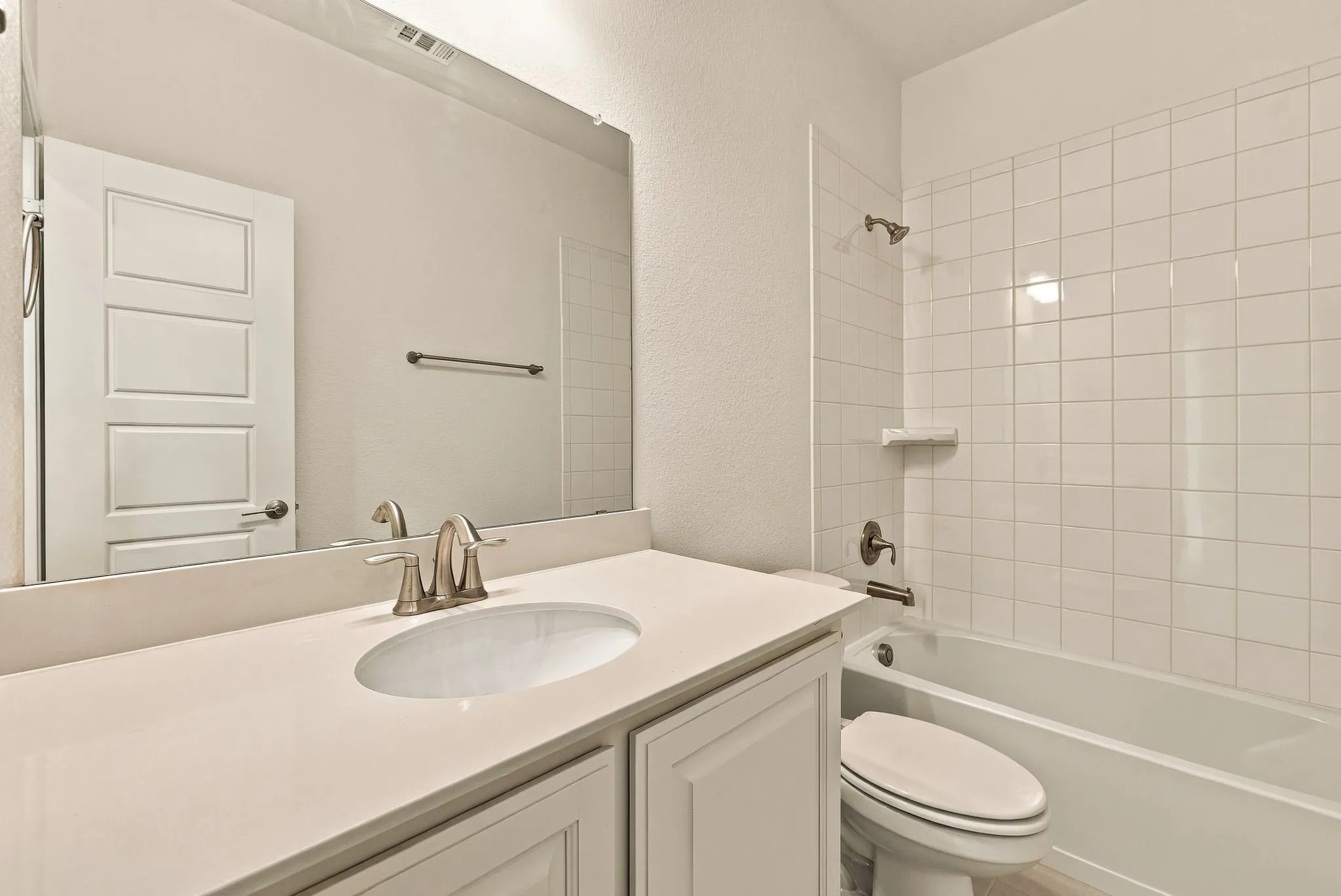 Bathroom featuring a vanity with a light-toned countertop, an undermount oval sink, a wall-to-wall mirror, and a tile-surround shower and tub combination