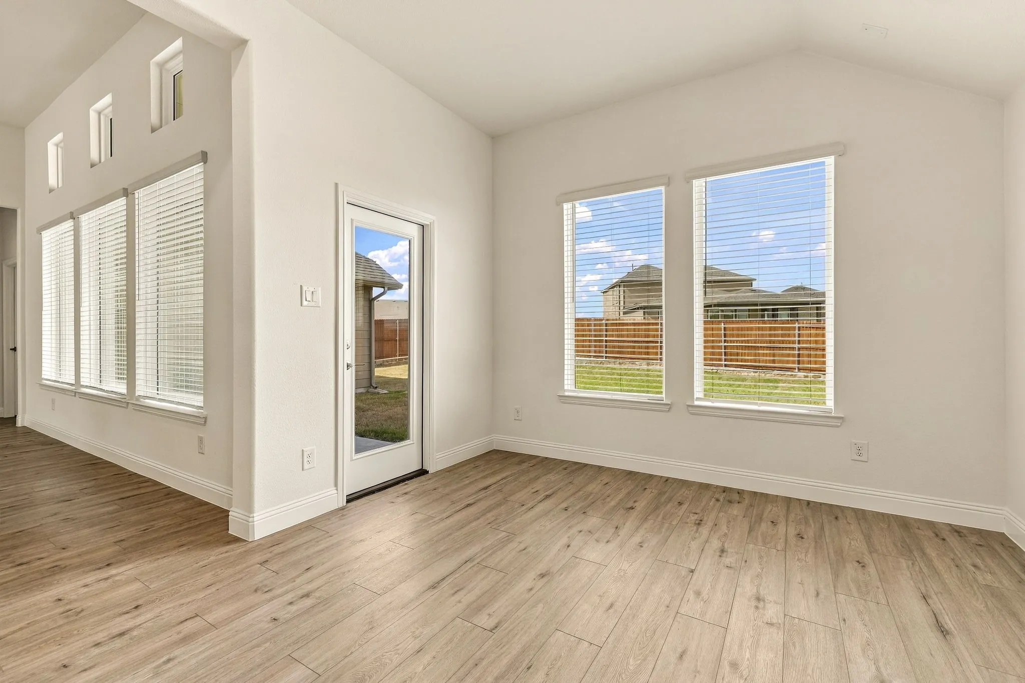 Vaulted ceilings featuring expansive windows, wood-finish flooring, and a glass-paneled exterior door
