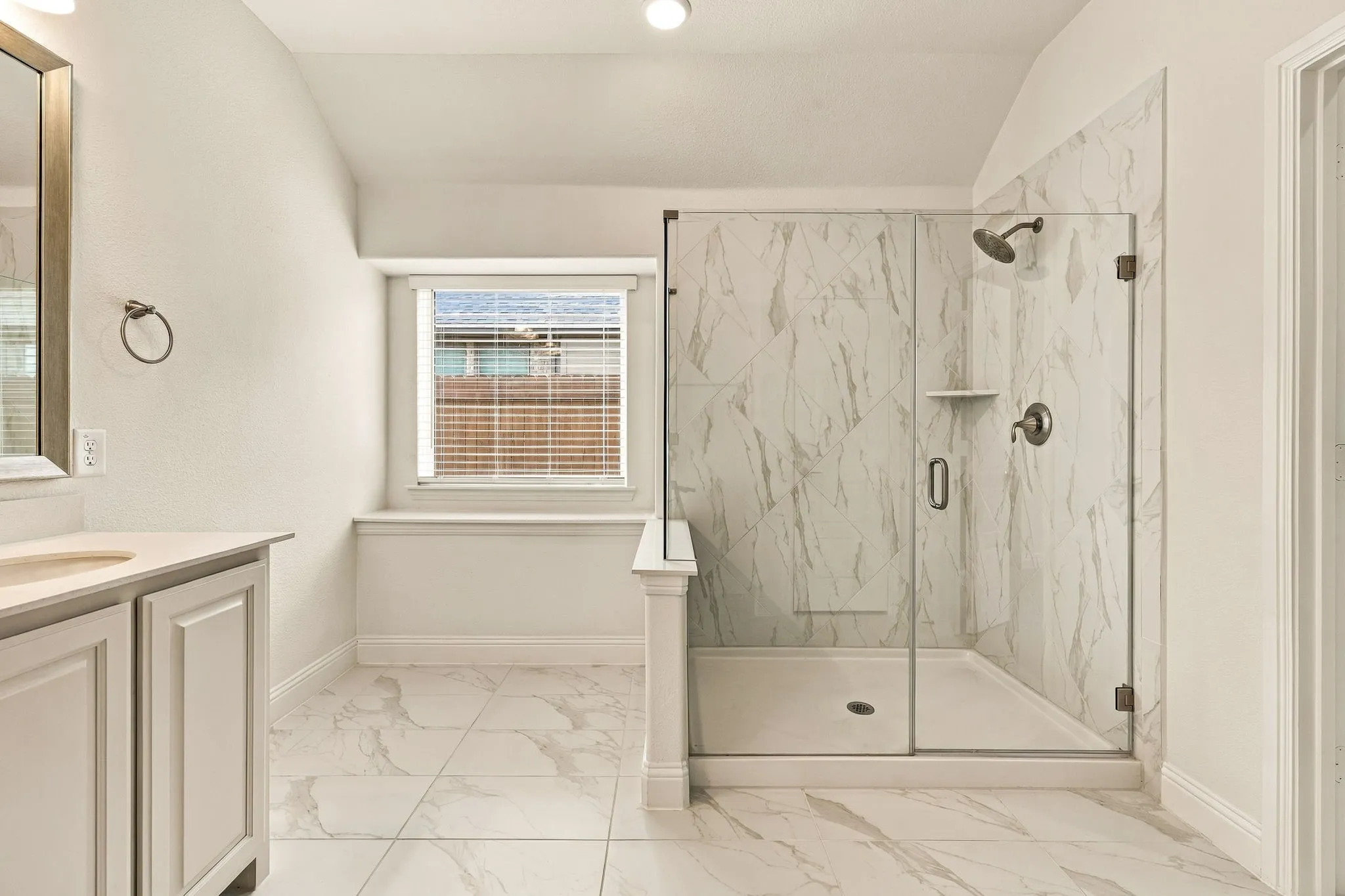 Walk-in glass-enclosed shower featuring large-format stone-patterned tile, white cabinetry with countertop, and matching floor tile