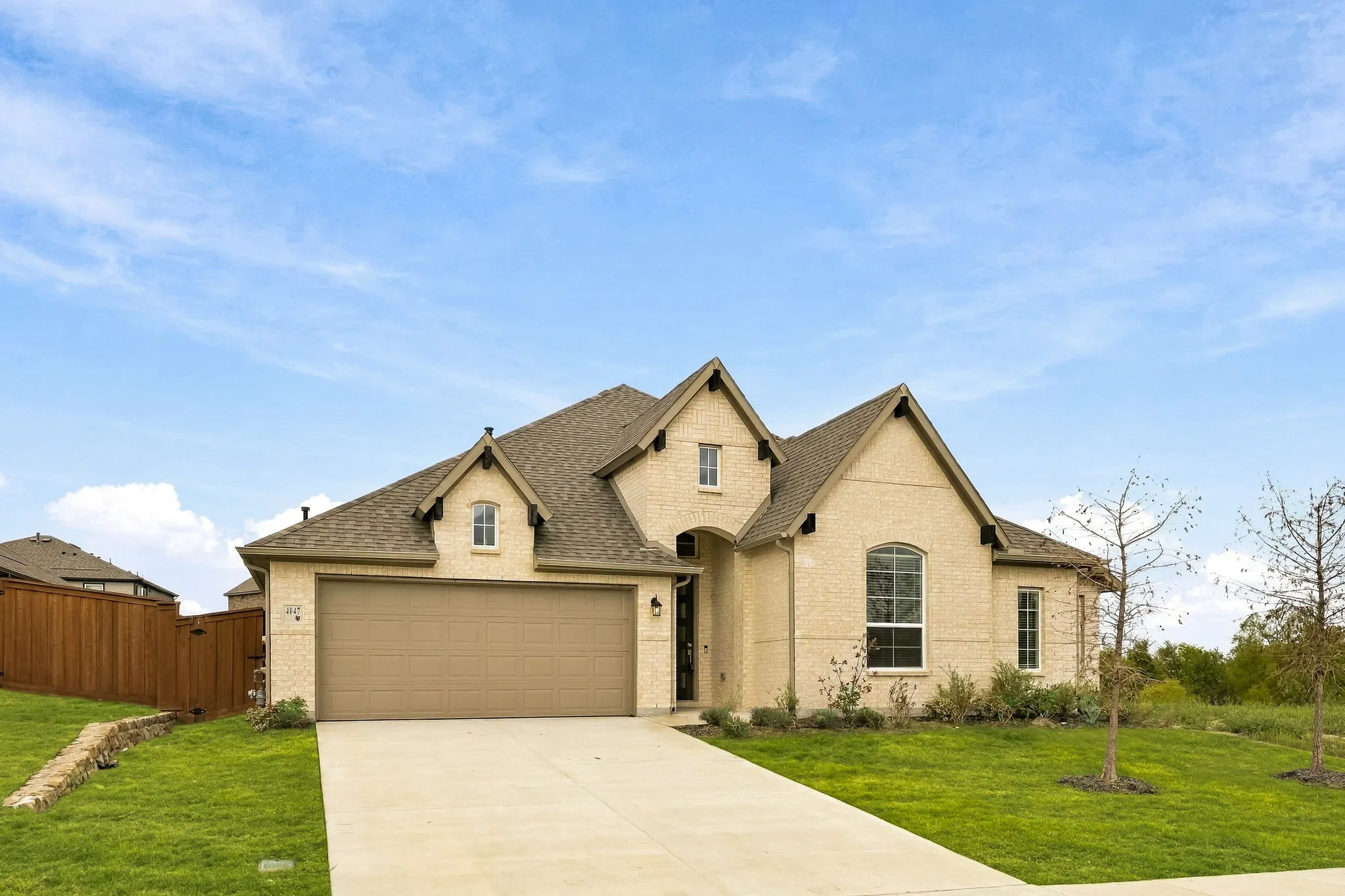 Brick and stone facade featuring a multi-gabled roofline, an attached two-car garage, and a concrete driveway