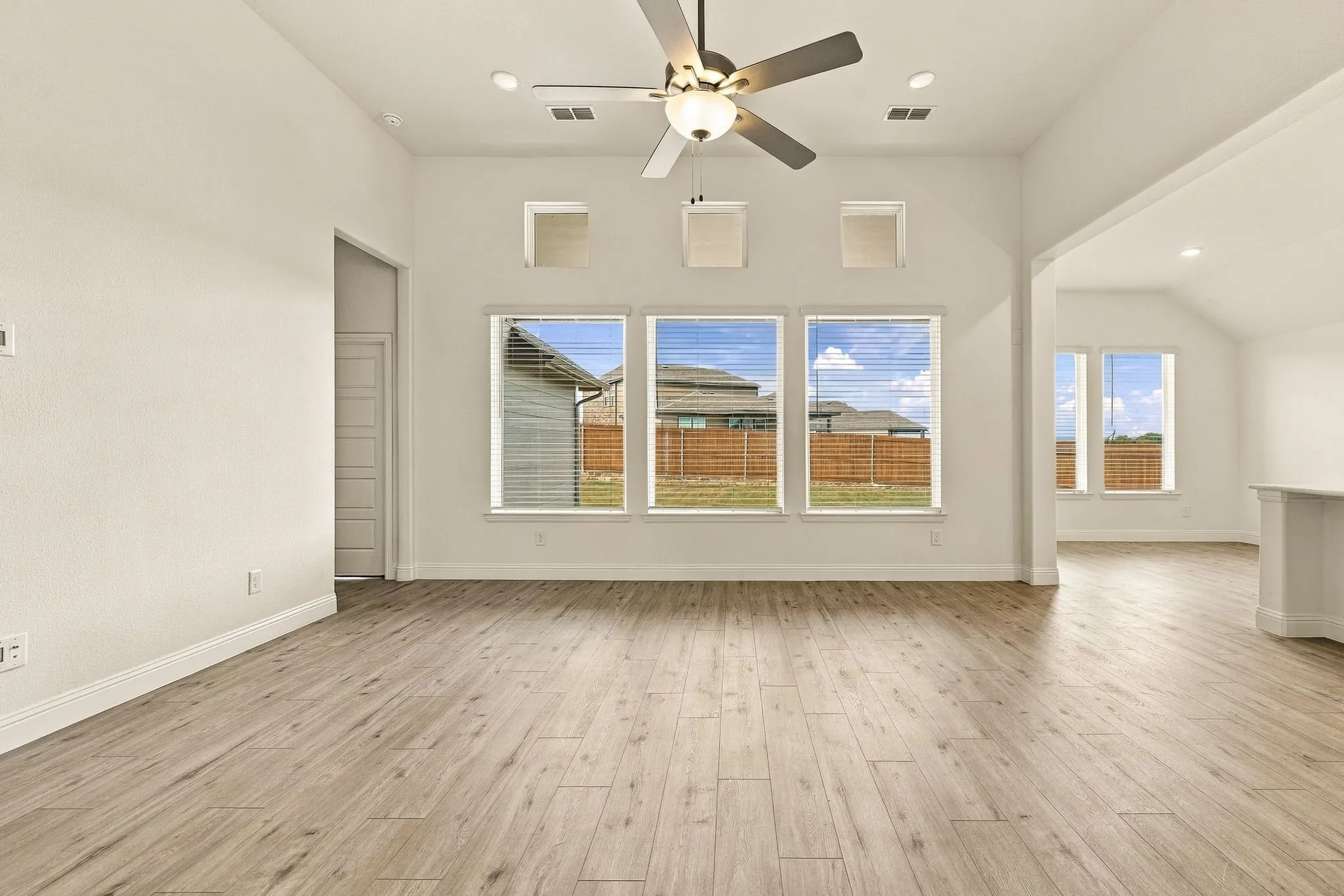 Vaulted ceilings featuring a central ceiling fan, wood-finish flooring, and expansive windows with transom detailing