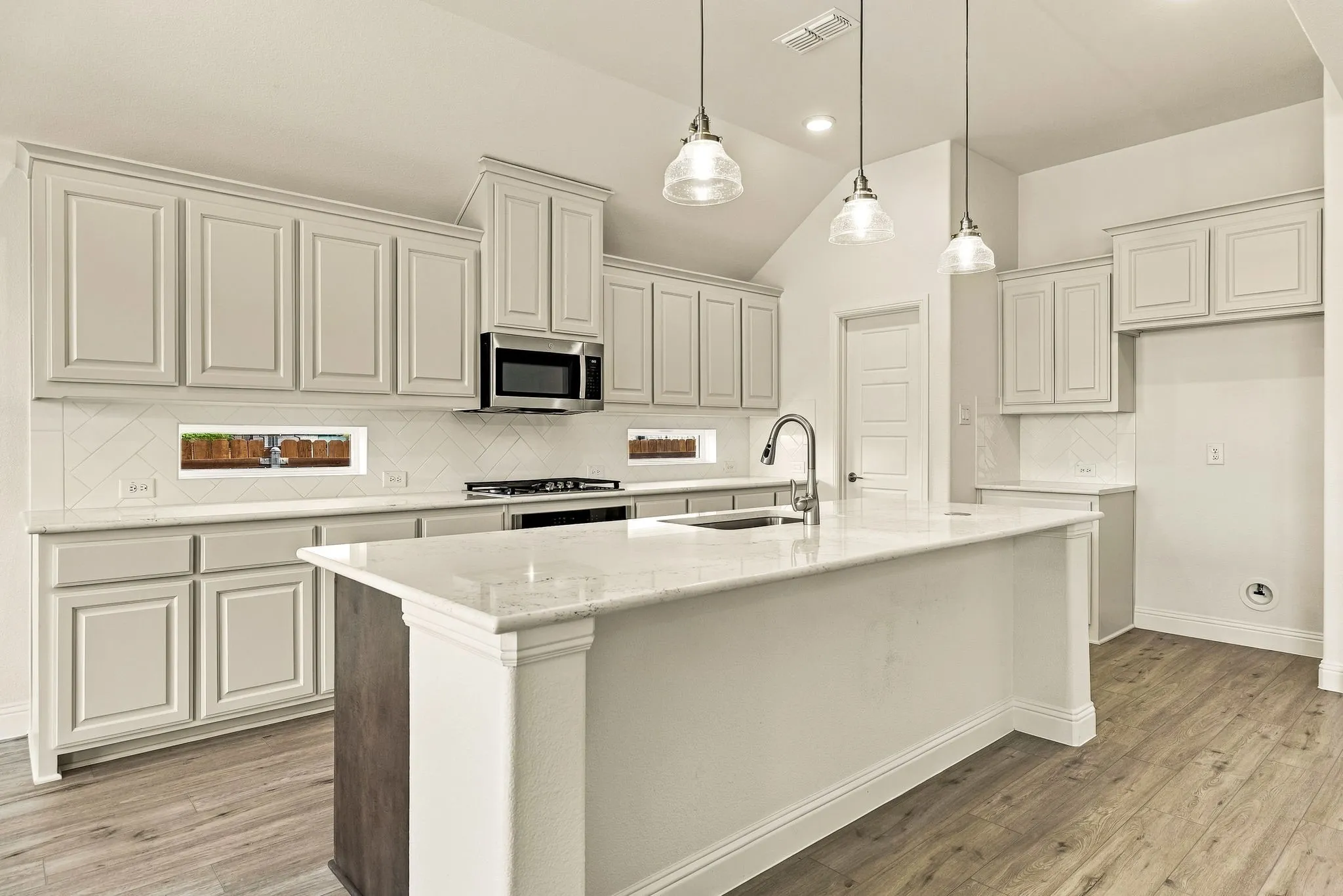 Kitchen featuring light-toned cabinetry, a central island with stone-finish countertops, stainless steel appliances, wood-finish flooring, and glass pendant lighting
