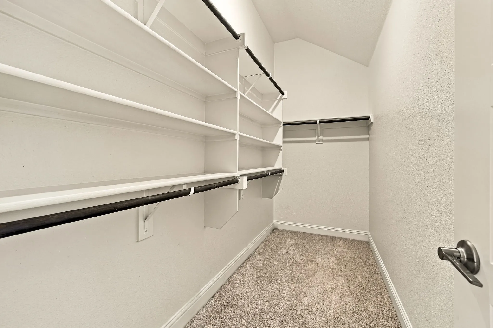 Walk-in closet featuring tiered white shelving, integrated hanging rods, and carpeted flooring