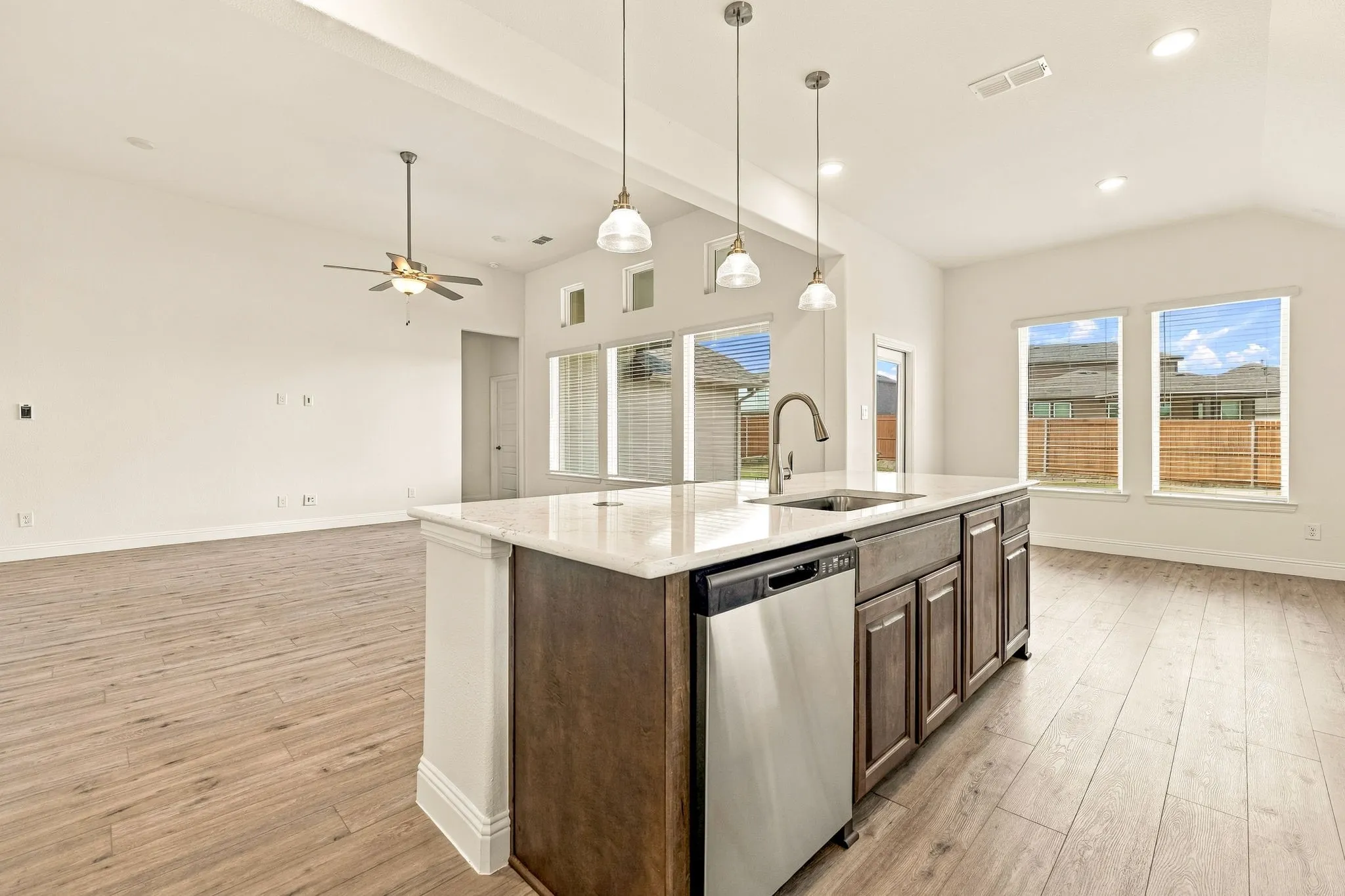 Kitchen island featuring stone countertops, integrated stainless steel dishwasher, undermount sink with gooseneck faucet, and dark-toned cabinetry, complemented by wood-finish flooring, vaulted ceilings, and pendant lighting
