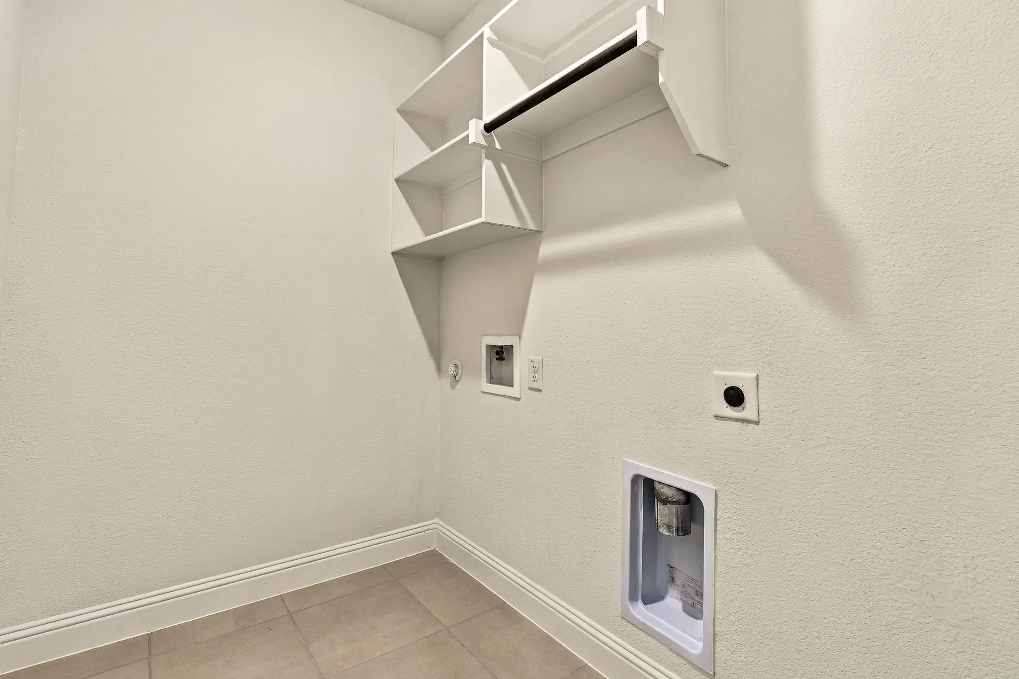 Utility space featuring neutral floor tiling, built-in shelving, a hanging rod, and dedicated washer and dryer hookups