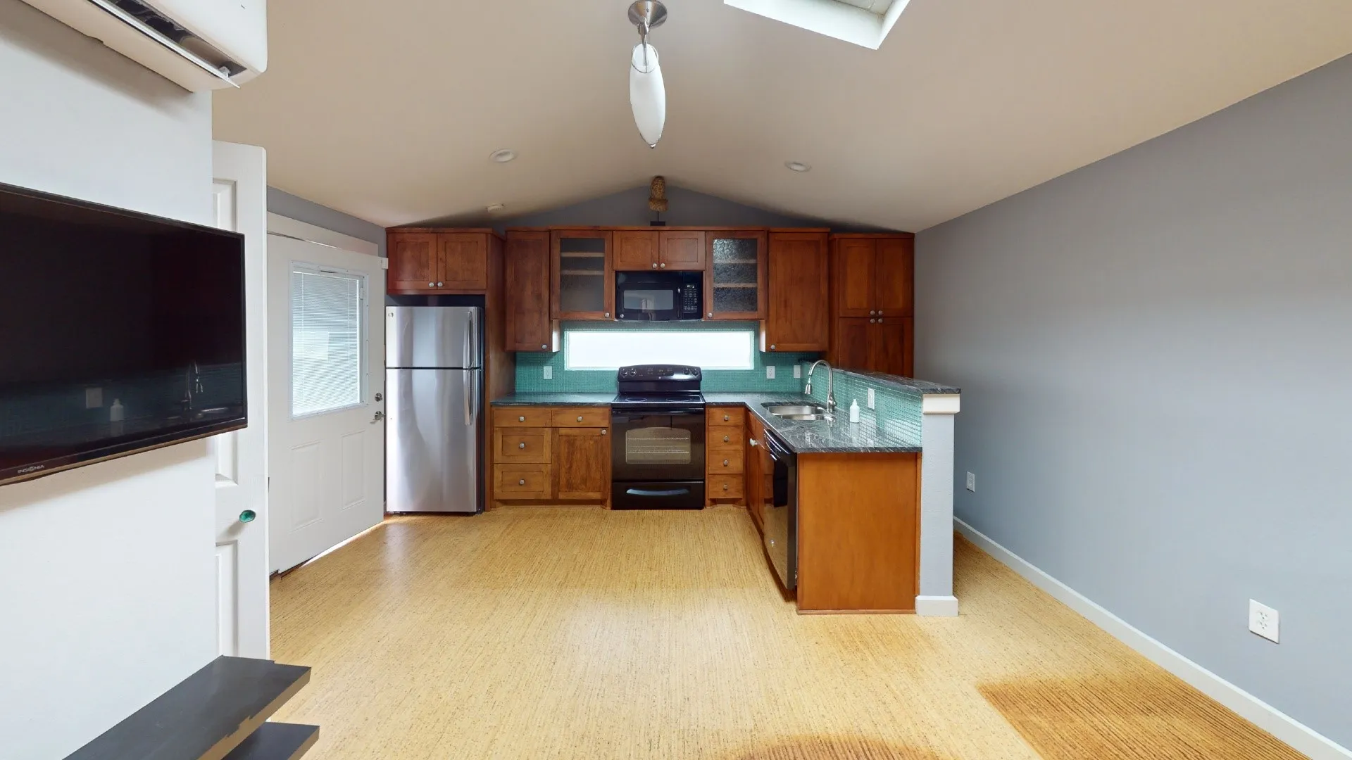 Kitchen featuring wood-finish cabinetry, stone-surface countertops, stainless steel refrigerator, black range, and wood-finish flooring under a vaulted ceiling