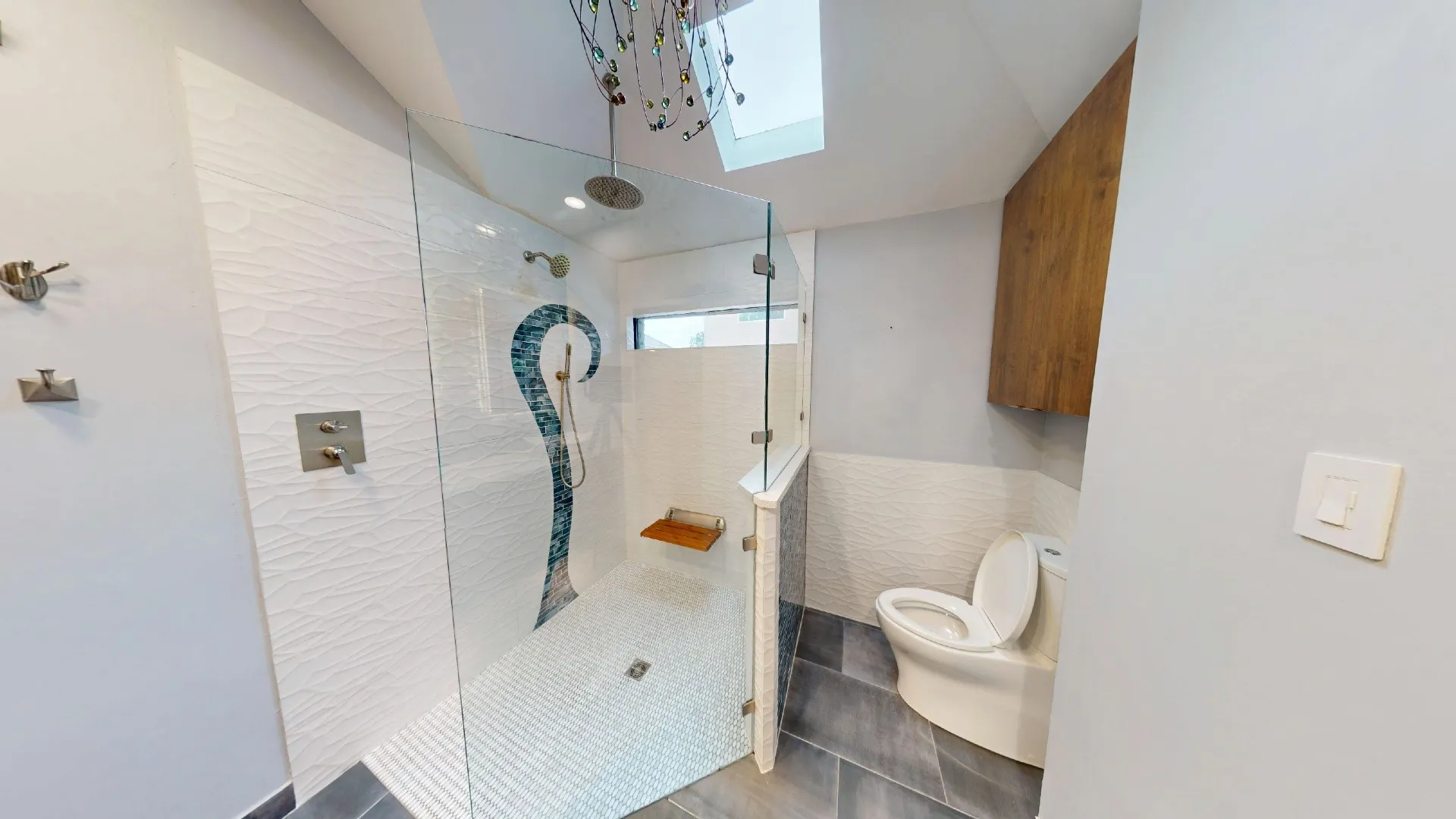 Walk-in shower featuring a frameless glass enclosure, rain showerhead, teak wood-finish fold-down seat, and textured tile walls with a mosaic decorative inlay