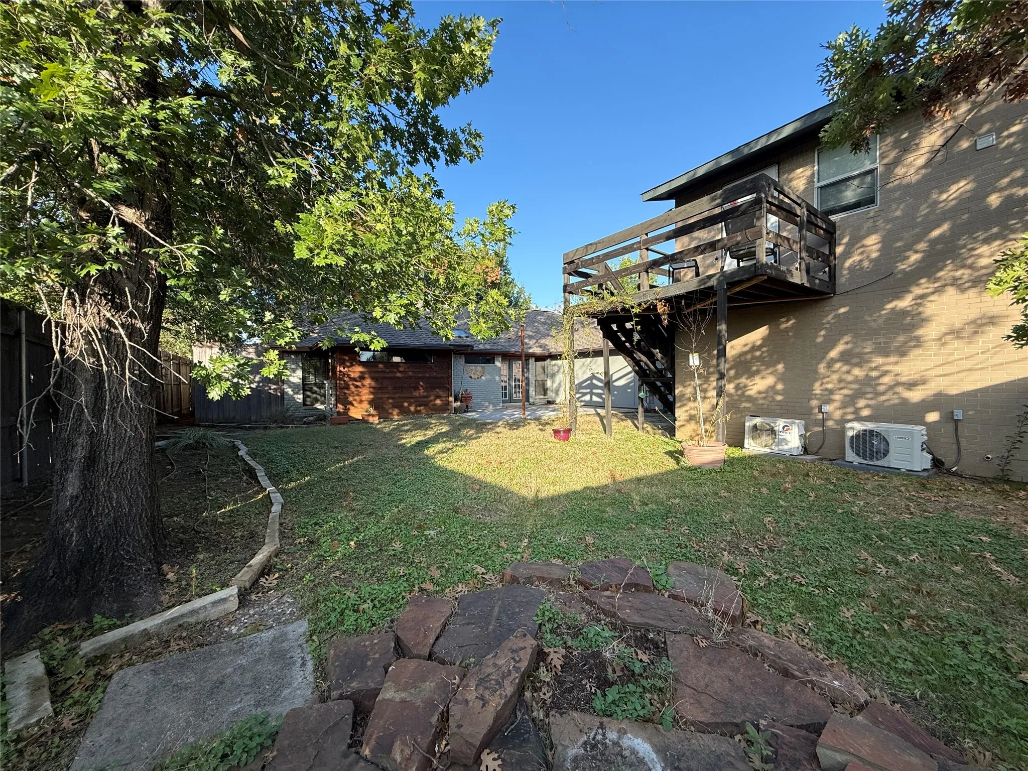 Backyard featuring a elevated wooden deck, stone hardscaping, mature trees, and a lawn area