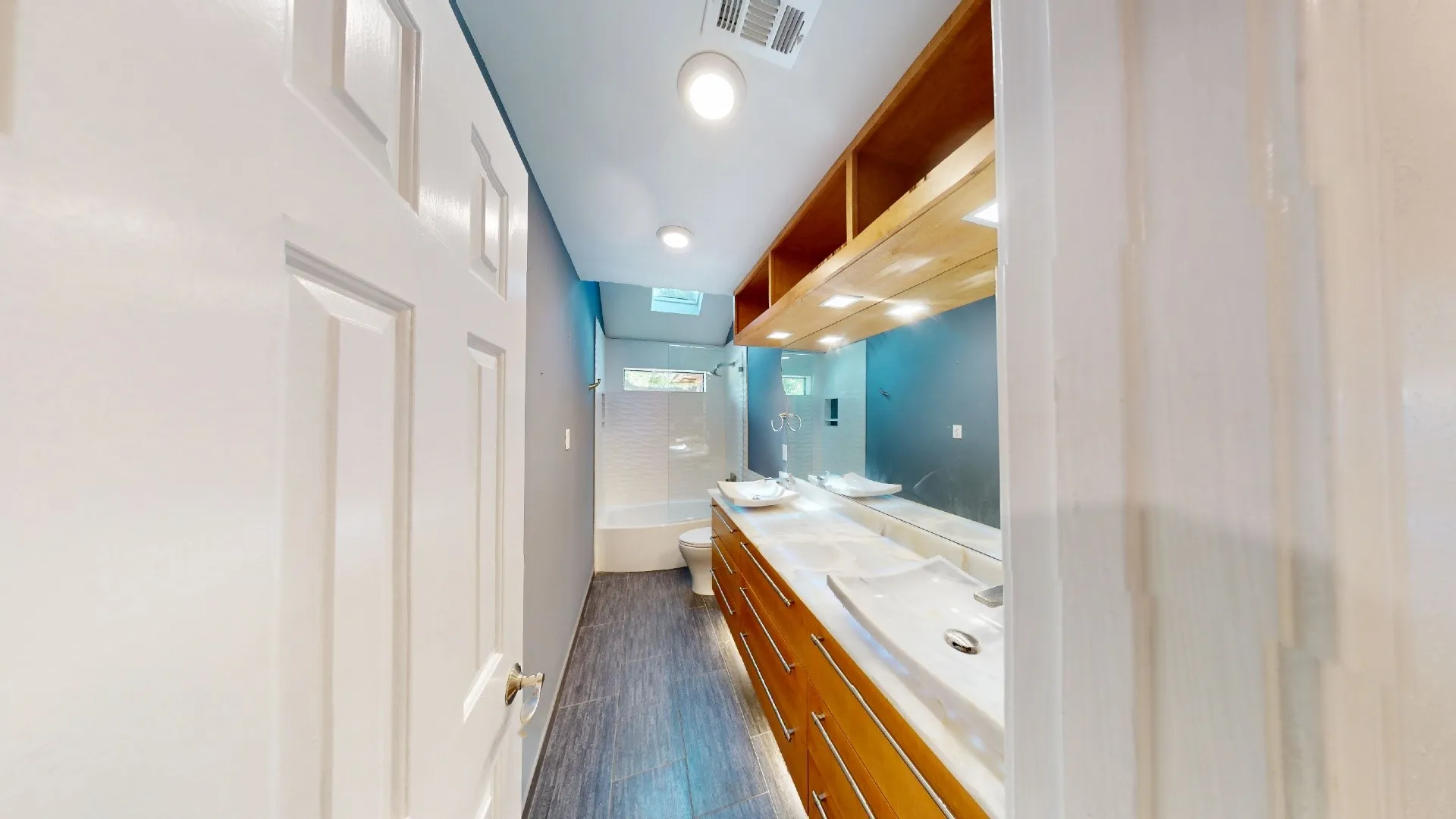 Double vanity featuring wood-finish cabinetry, rectangular vessel sinks, extensive wall-to-wall mirror, built-in overhead shelving, and tile flooring