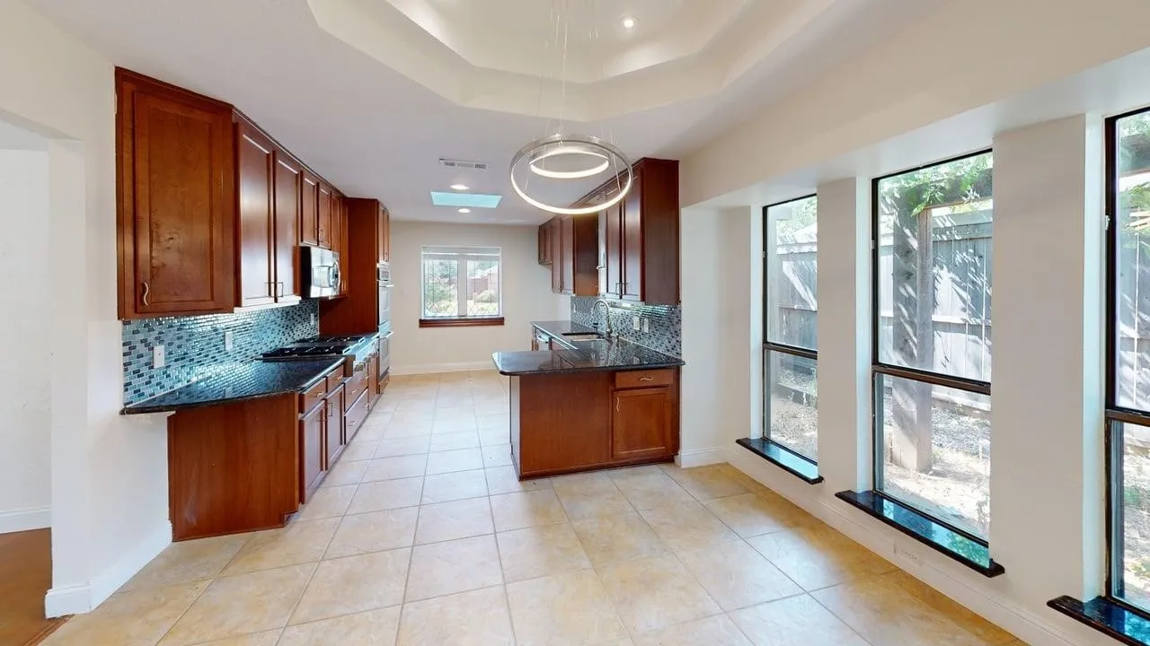 Kitchen featuring custom wood cabinetry, dark stone countertops, decorative glass tile backsplash, tray ceiling, and floor-to-ceiling windows