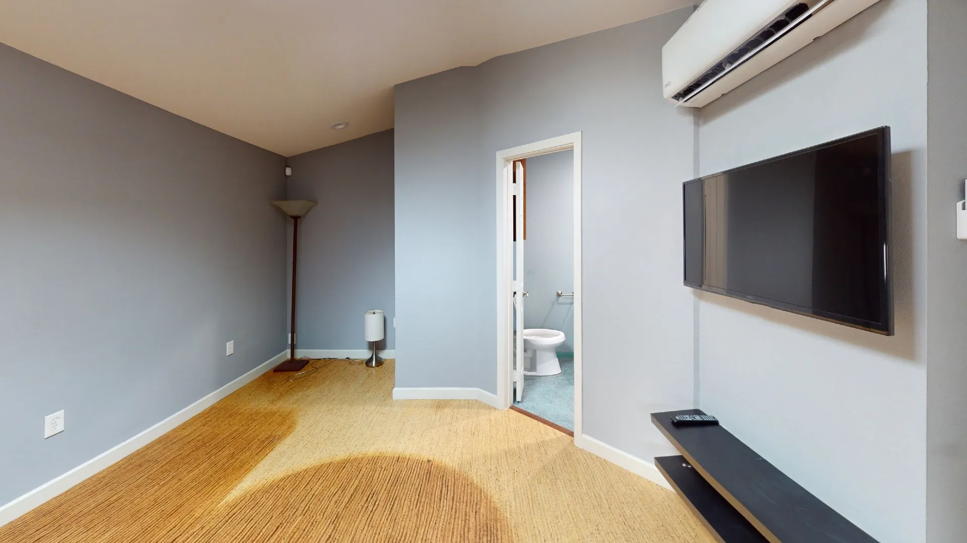Neutral-toned interior featuring wood-finish flooring, a wall-mounted ductless mini-split system, and a floating shelving unit