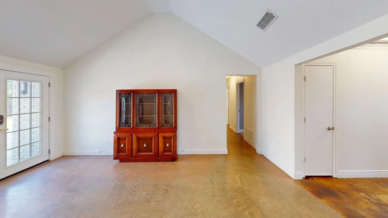 Spacious room featuring soaring vaulted ceilings, wood-finish flooring throughout, and abundant natural light from multiple windows and glass doors