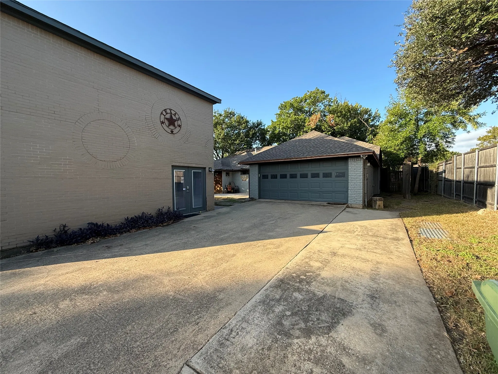 Painted brick exterior featuring a multi-car garage, concrete driveway, and wooden privacy fencing