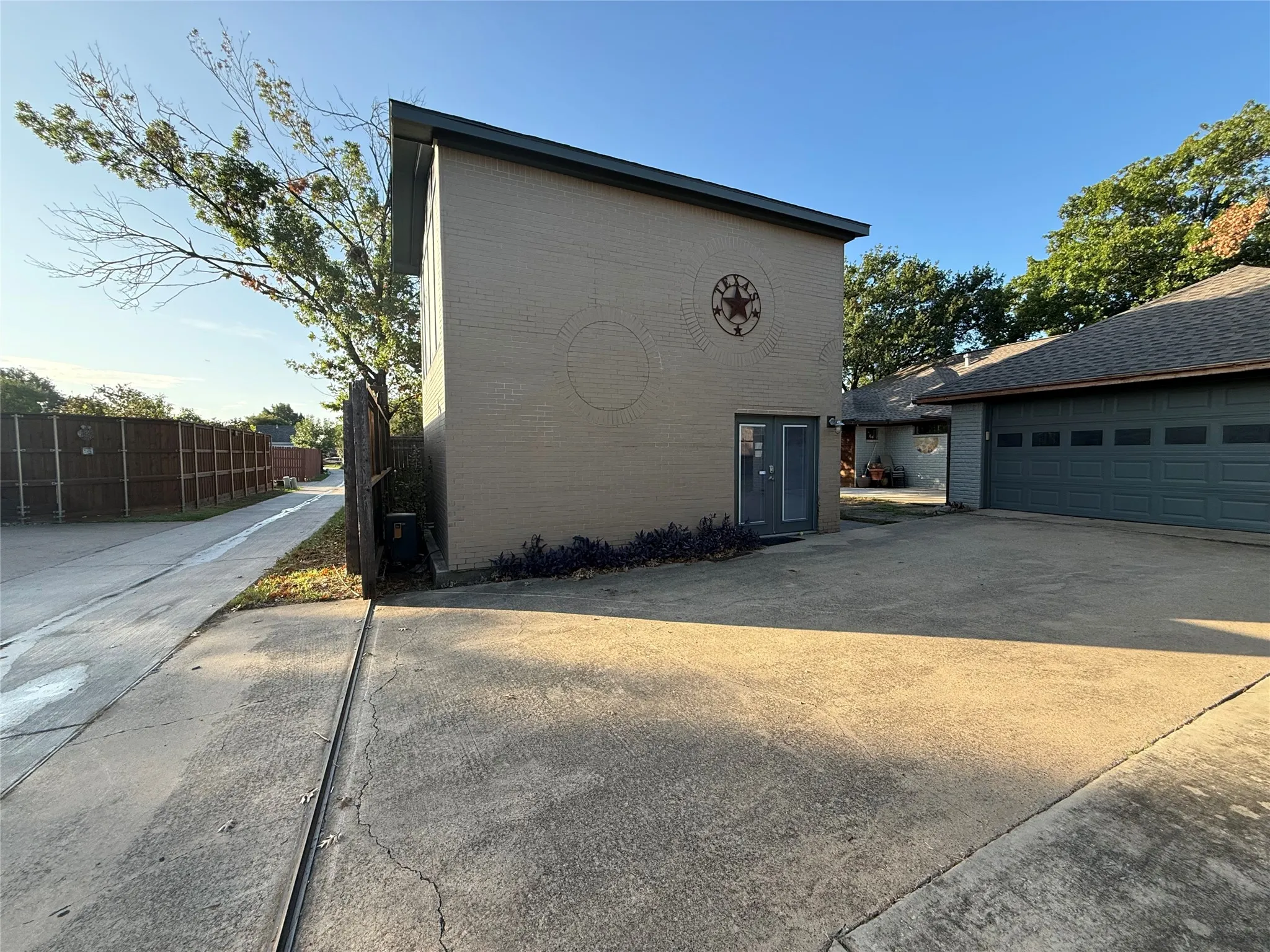 Two-story brick structure featuring glass-paneled entry doors, concrete parking surface, and wood-slat perimeter fencing