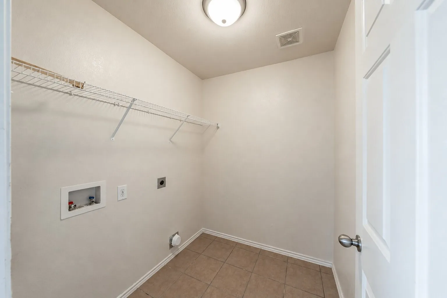 Utility space featuring ceramic tile flooring, built-in wire shelving, and dedicated hookups for laundry appliances
