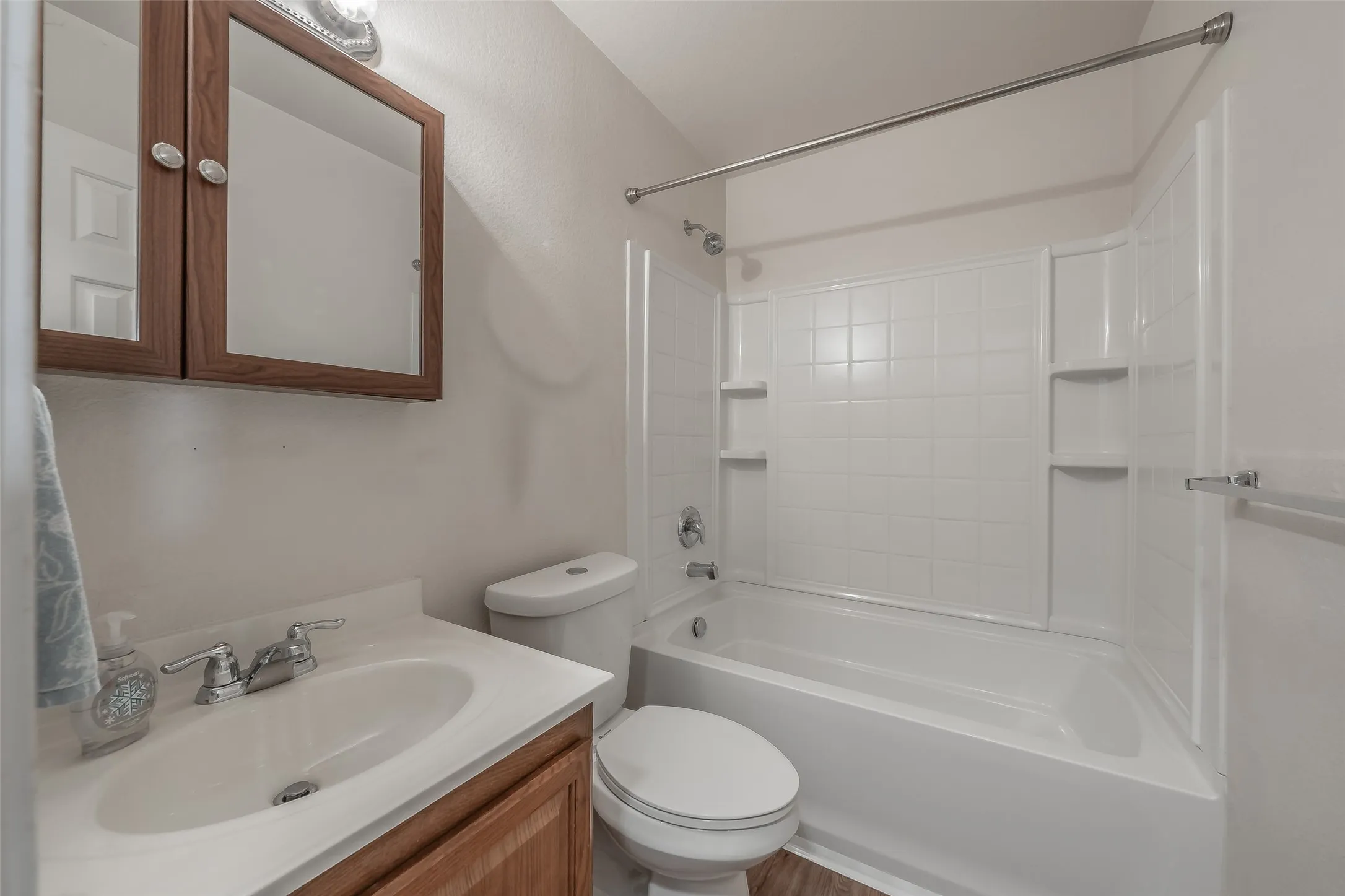 White vanity with an integrated sink and chrome faucet, wood-finish cabinetry, and a mirrored medicine cabinet