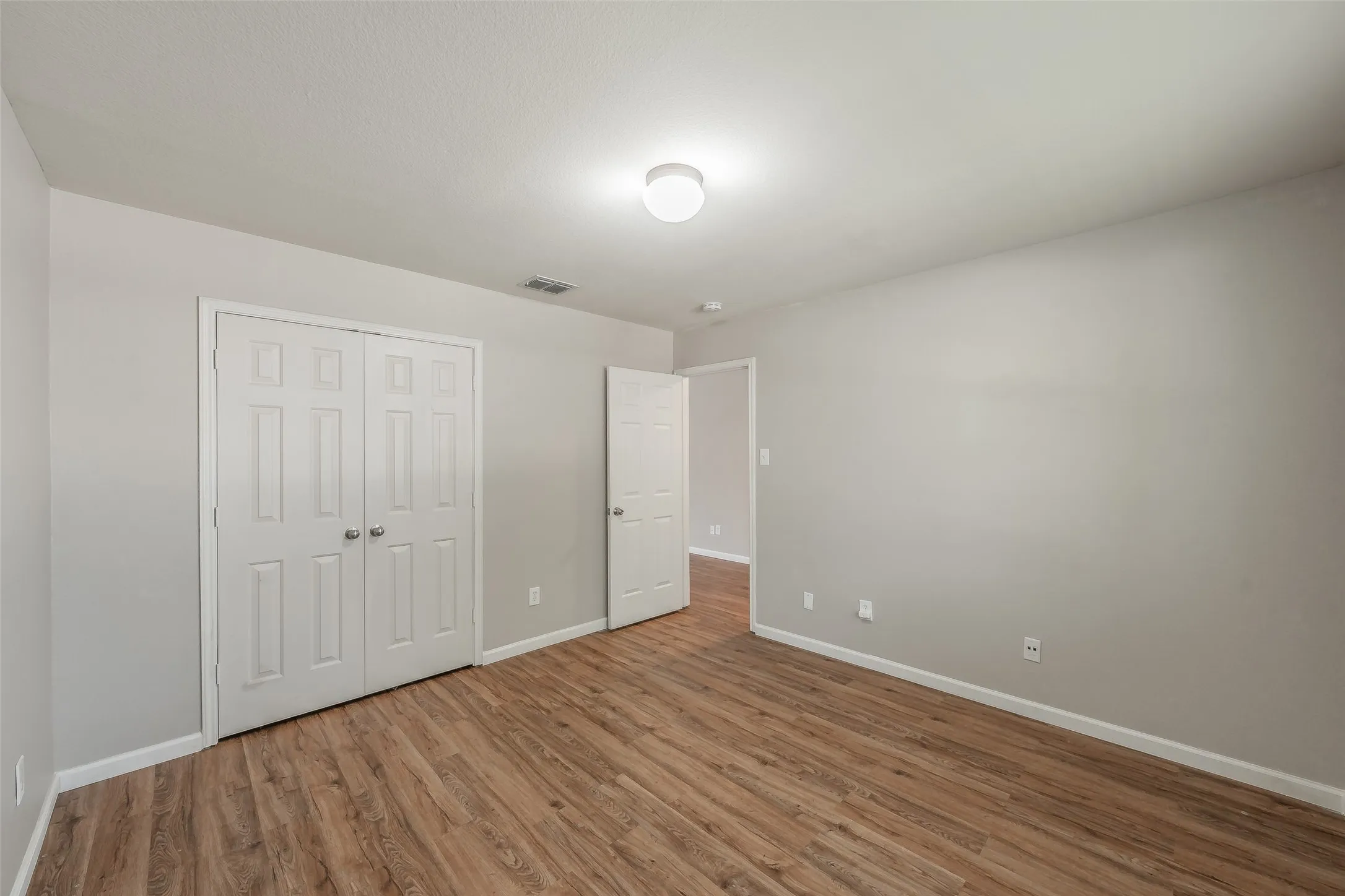 Wood-finish flooring throughout, light gray wall paint, white trim, recessed lighting, and a white six-panel door