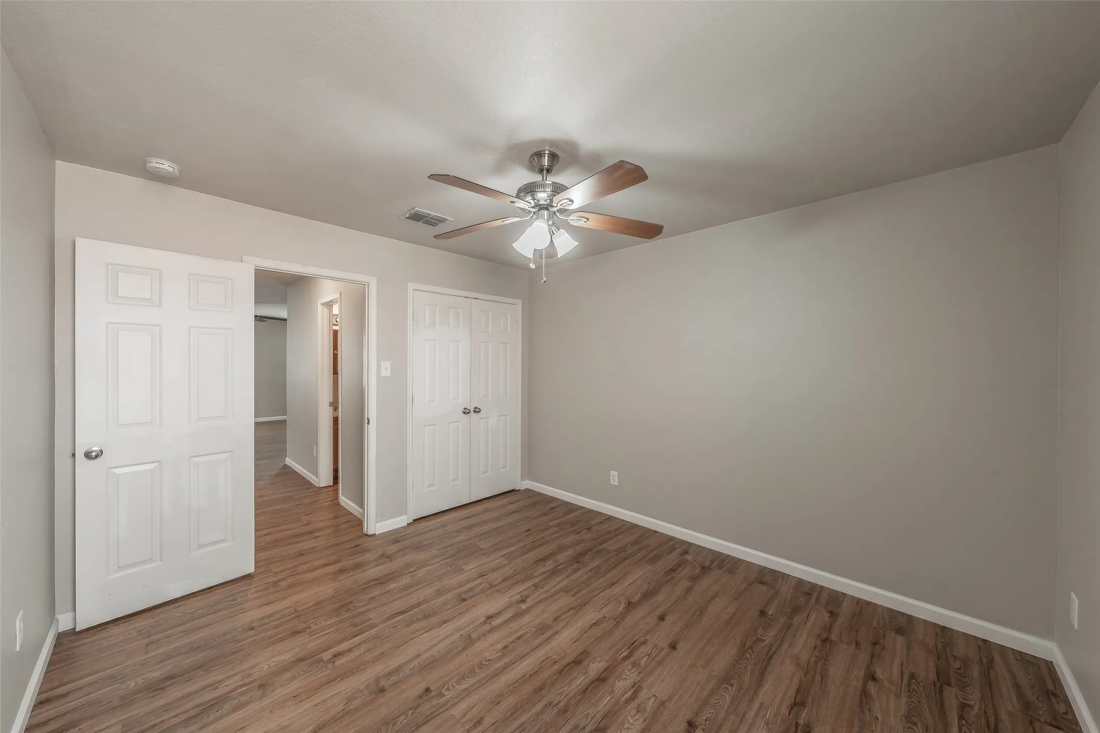 Wood-finish flooring, neutral wall tones, ceiling fan with light fixture, and white bi-fold closet doors