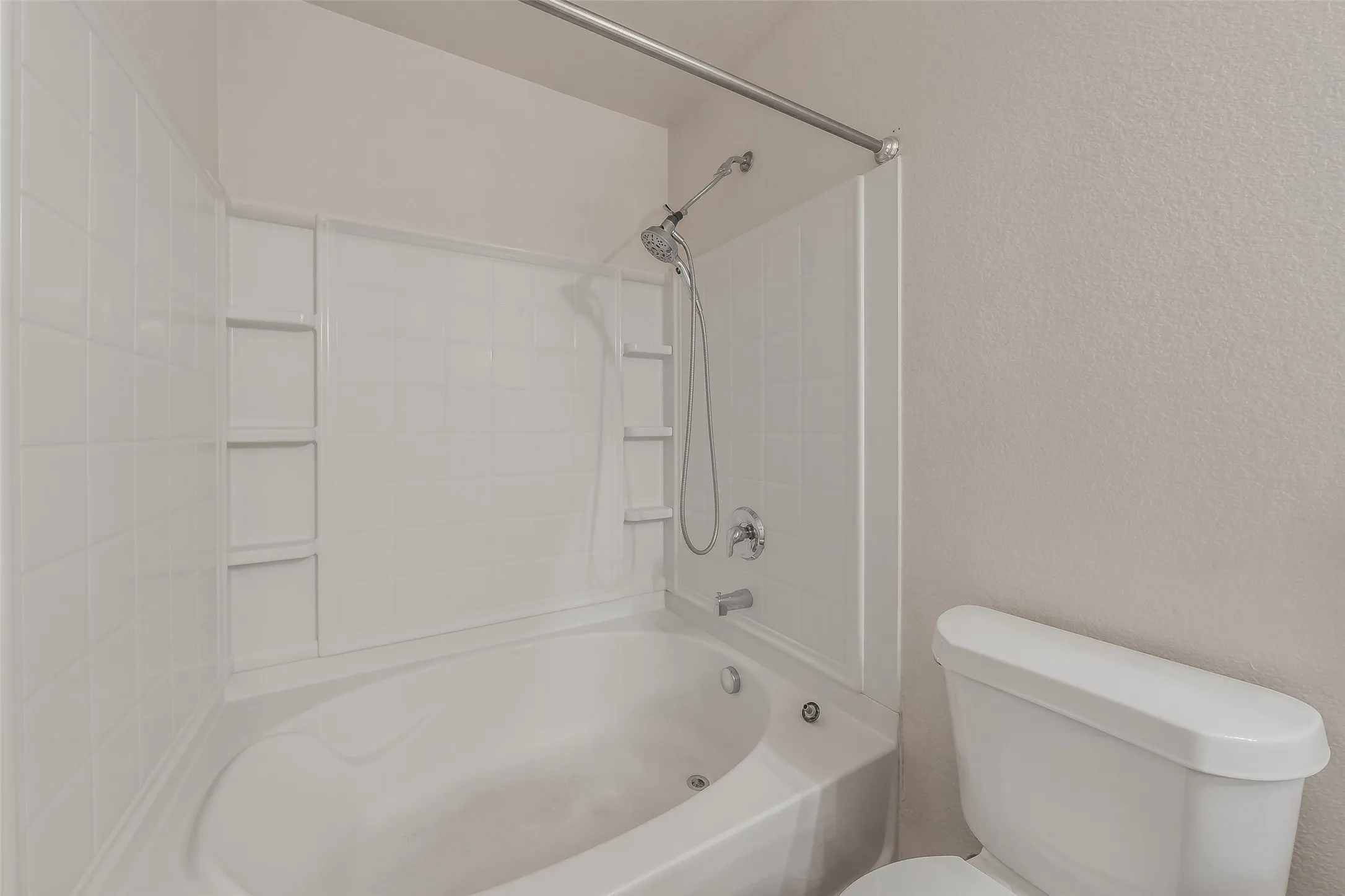 Bathtub with integrated shower, white tile-patterned shower surround, and a toilet with a white tank and bowl