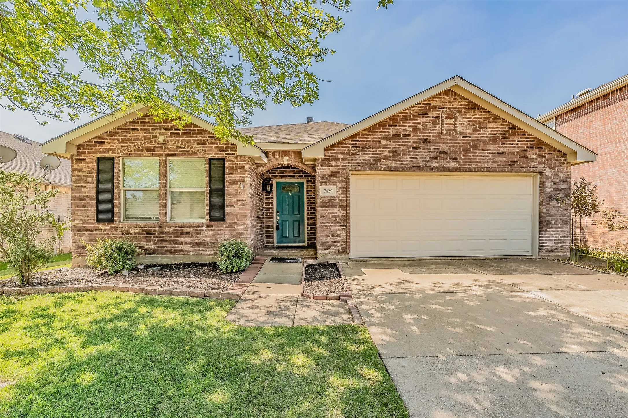 Brick exterior with a gabled roofline, attached garage, concrete driveway, and front landscaping