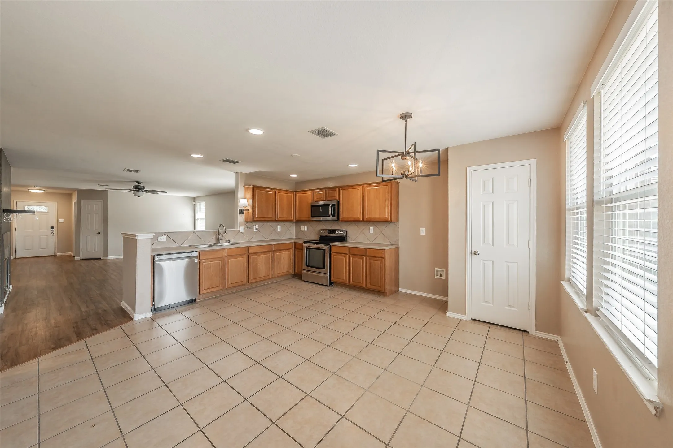 Kitchen featuring wood-finish cabinetry, stainless steel appliances, tiled backsplash, and an angular chandelier