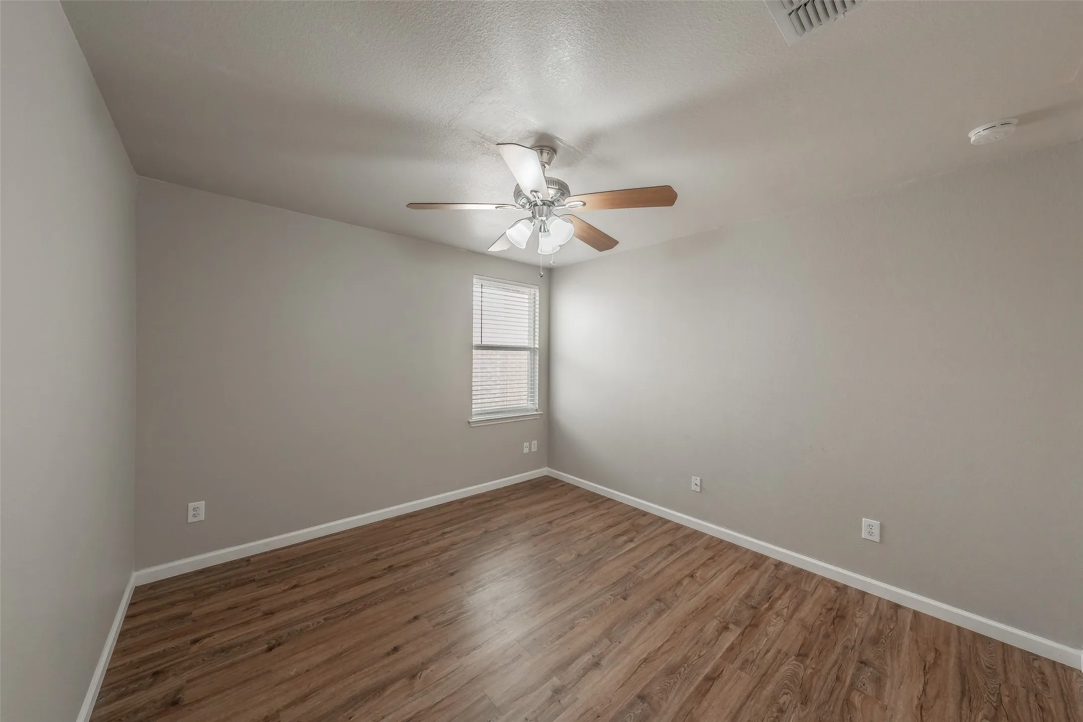 Wood-finish flooring, single window with blinds, ceiling fan with light fixture, and light gray wall paint