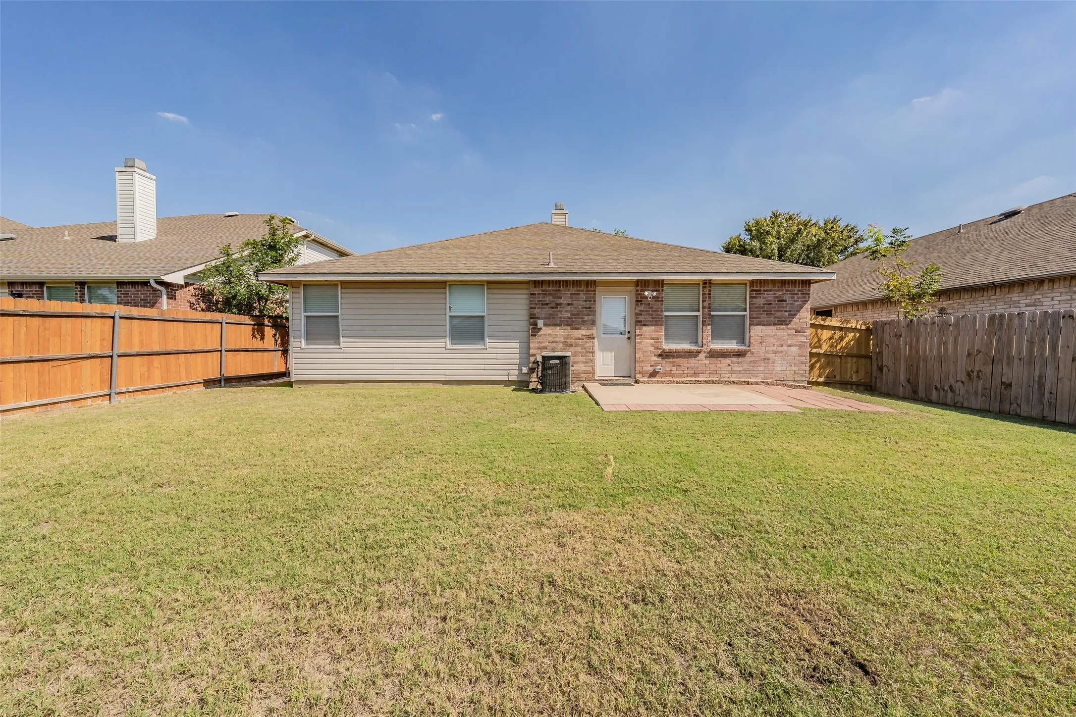 Expansive backyard with a manicured lawn, brick exterior, split-rail fencing, and a concrete patio