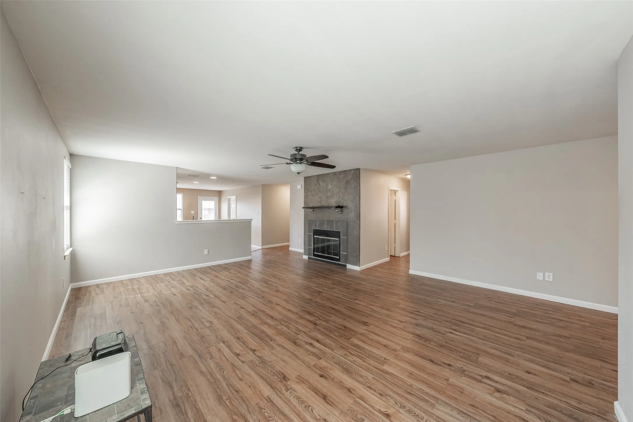 Expansive room featuring wood-finish flooring, a textured stone fireplace with a black insert, and a ceiling fan