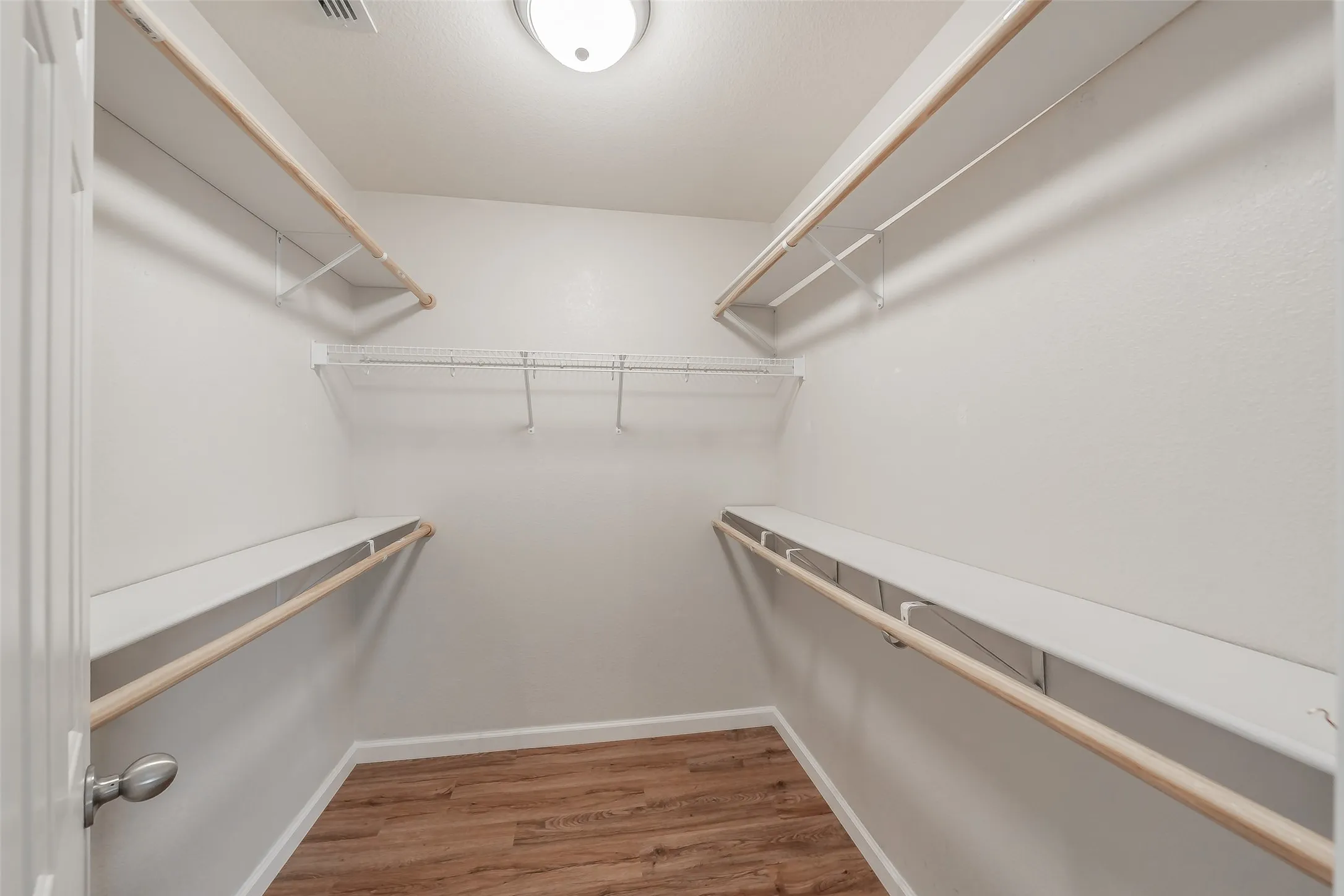 Walk-in closet featuring wood-finish flooring, multiple shelving units, and a ceiling-mounted light fixture