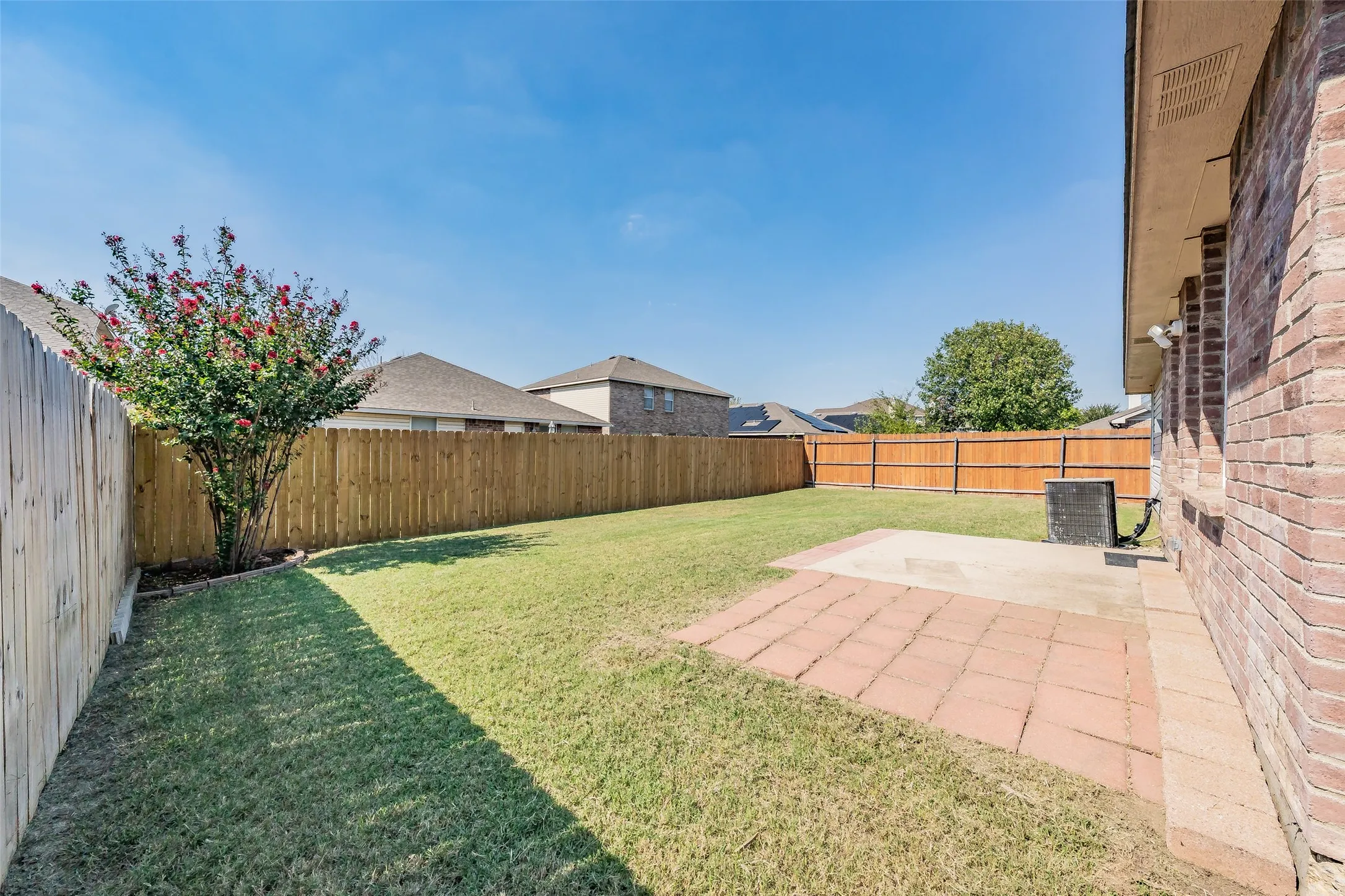 Private backyard with wood fencing, a brick exterior wall, a paver patio, and a mature tree