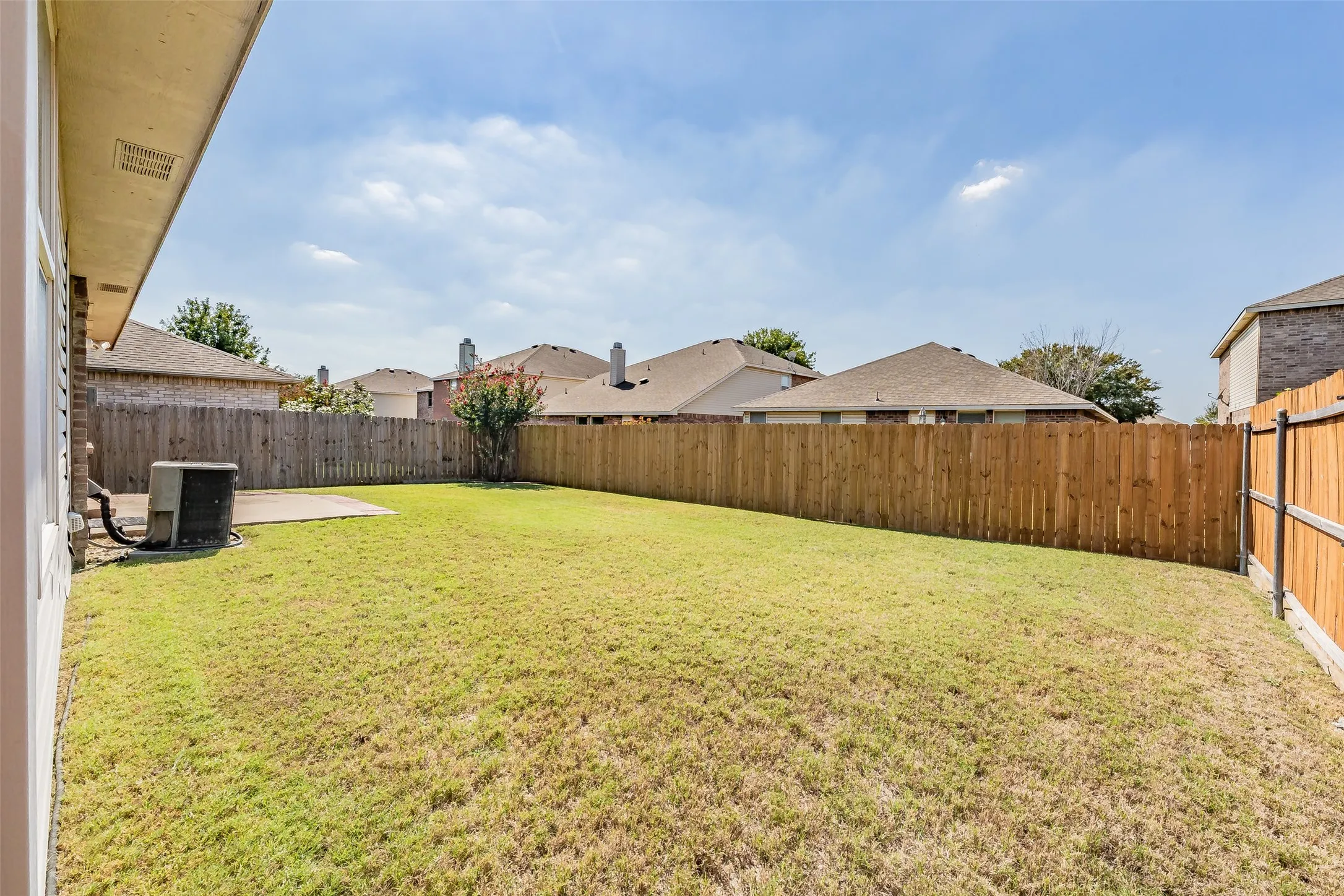 Expansive backyard with a manicured lawn, full-height privacy fencing, and a concrete patio