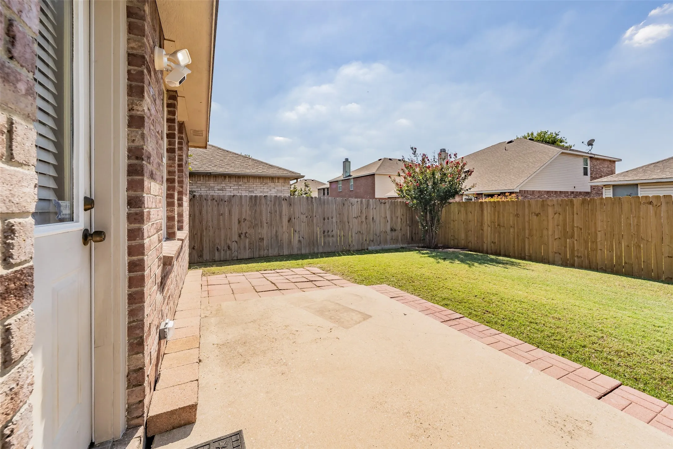 Private backyard with a wood privacy fence, a concrete patio bordered by brick, and a manicured lawn