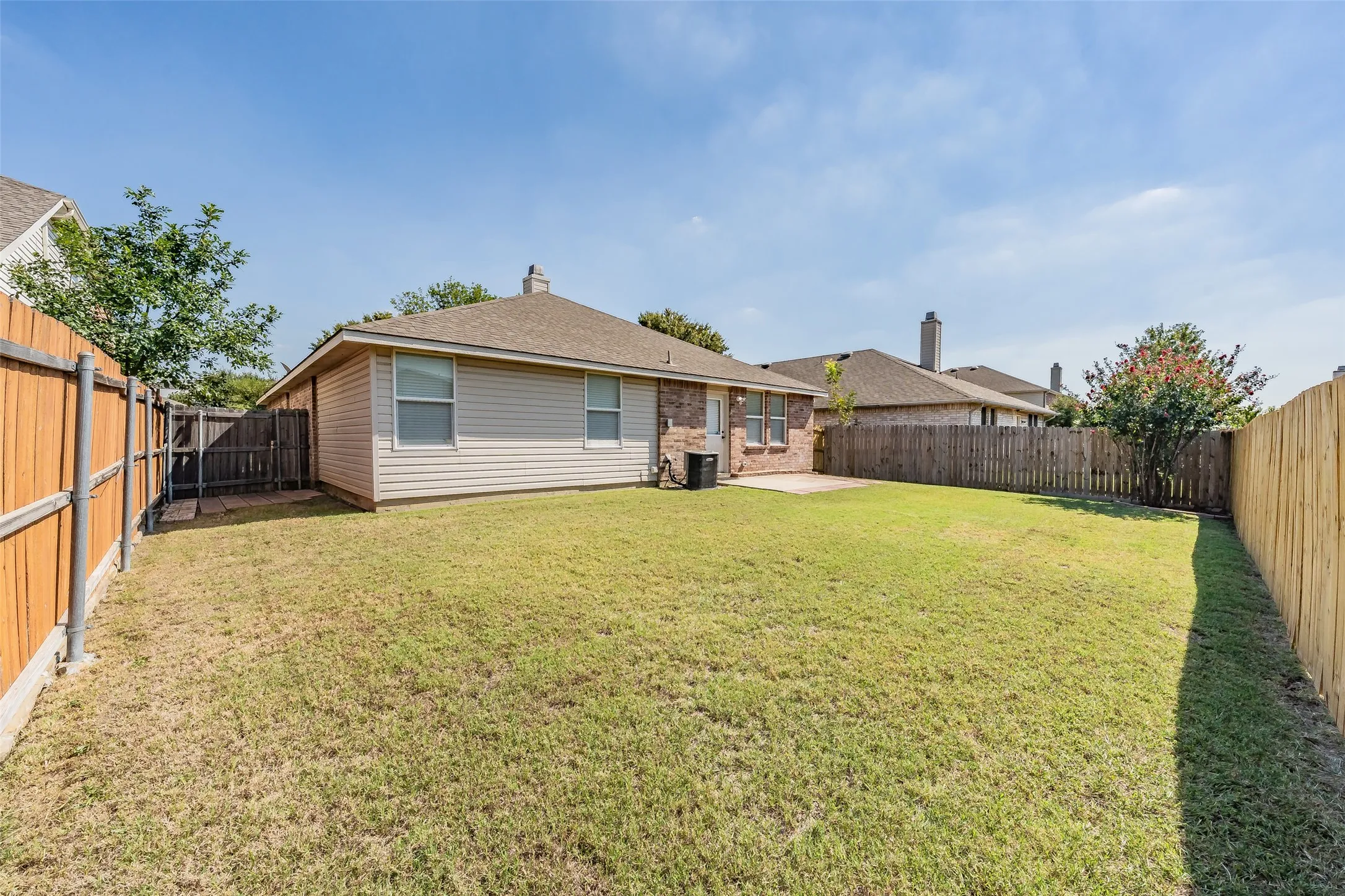 Expansive backyard with a manicured lawn, wood fencing, and a concrete patio