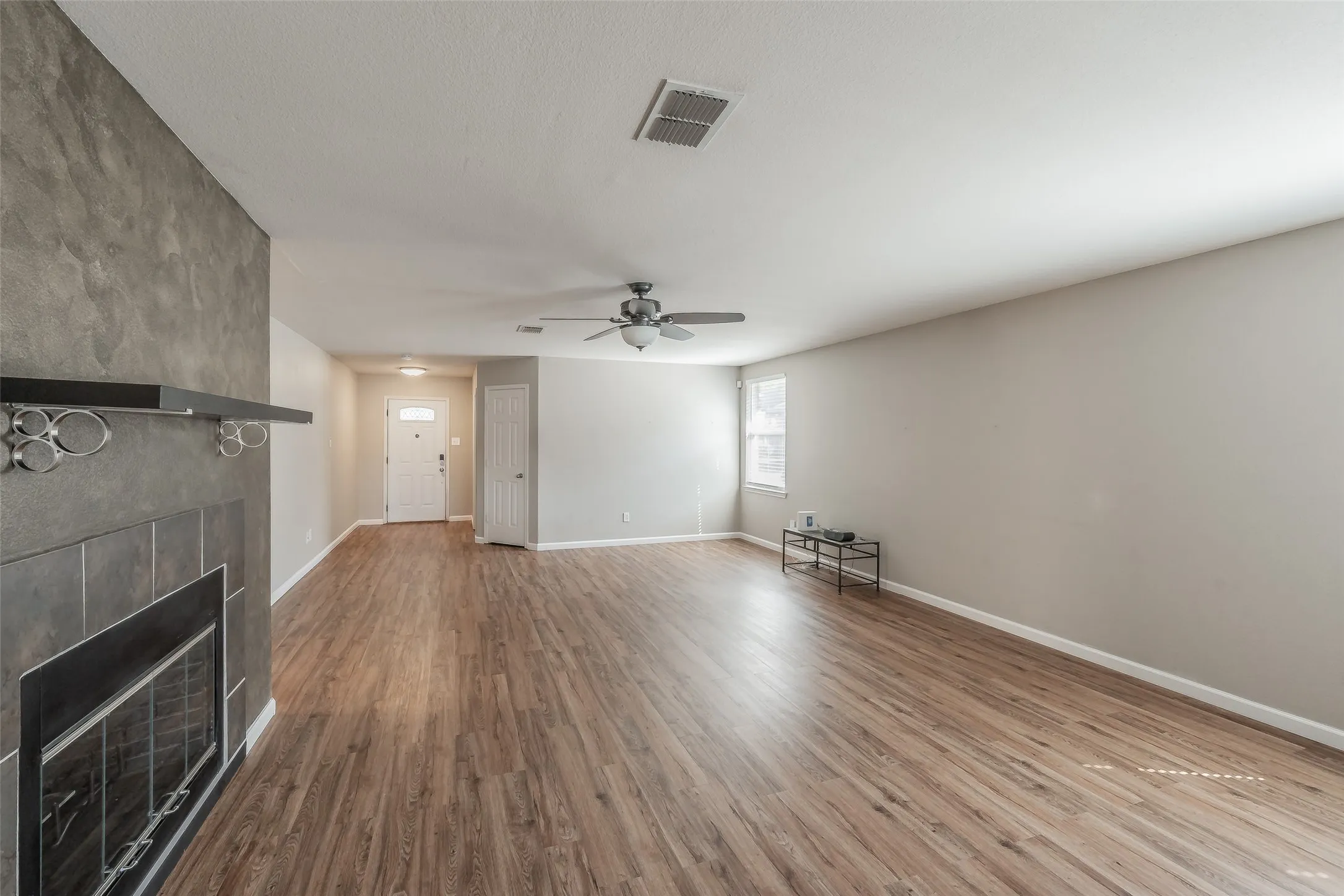 Open-concept living area featuring wood-finish flooring, a fireplace with a dark tile surround, a built-in mantel, and a ceiling fan