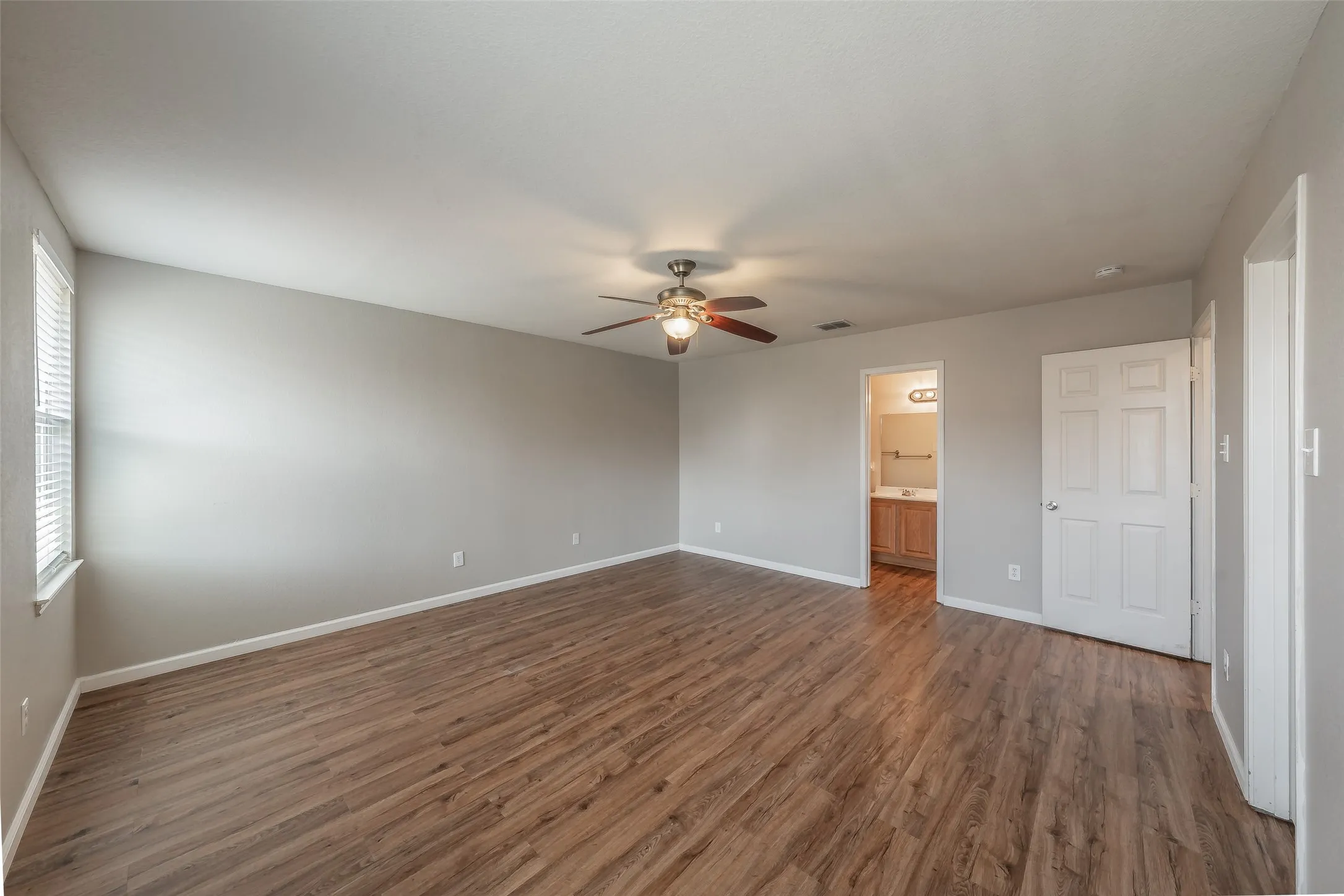 Spacious room featuring wood-finish flooring, a ceiling fan with integrated lighting, and multiple windows with blinds