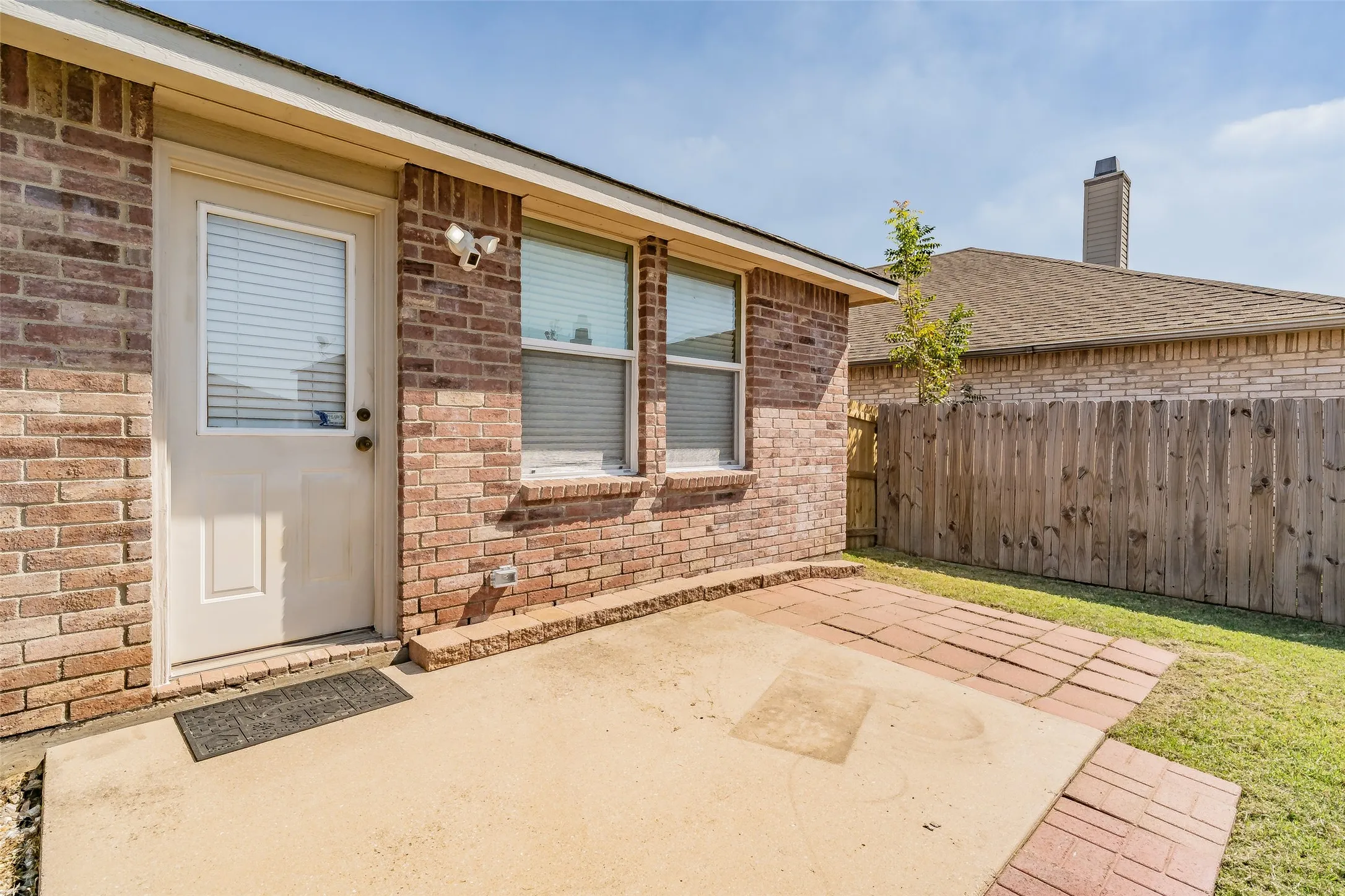 Brick exterior featuring a concrete patio, a wooden privacy fence, and a manicured lawn