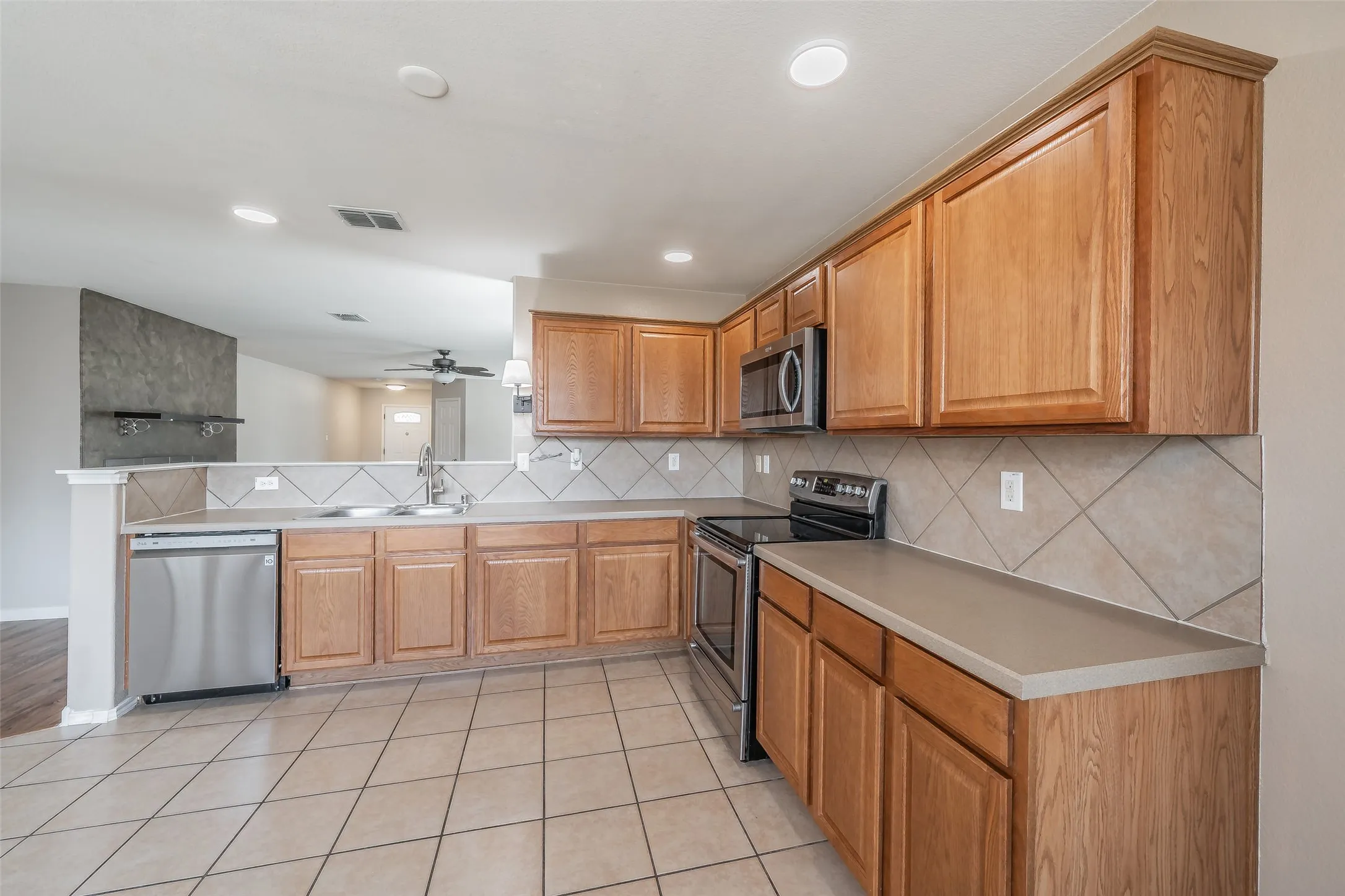 Kitchen with wood cabinetry, stainless steel appliances, tile flooring, and a tile backsplash