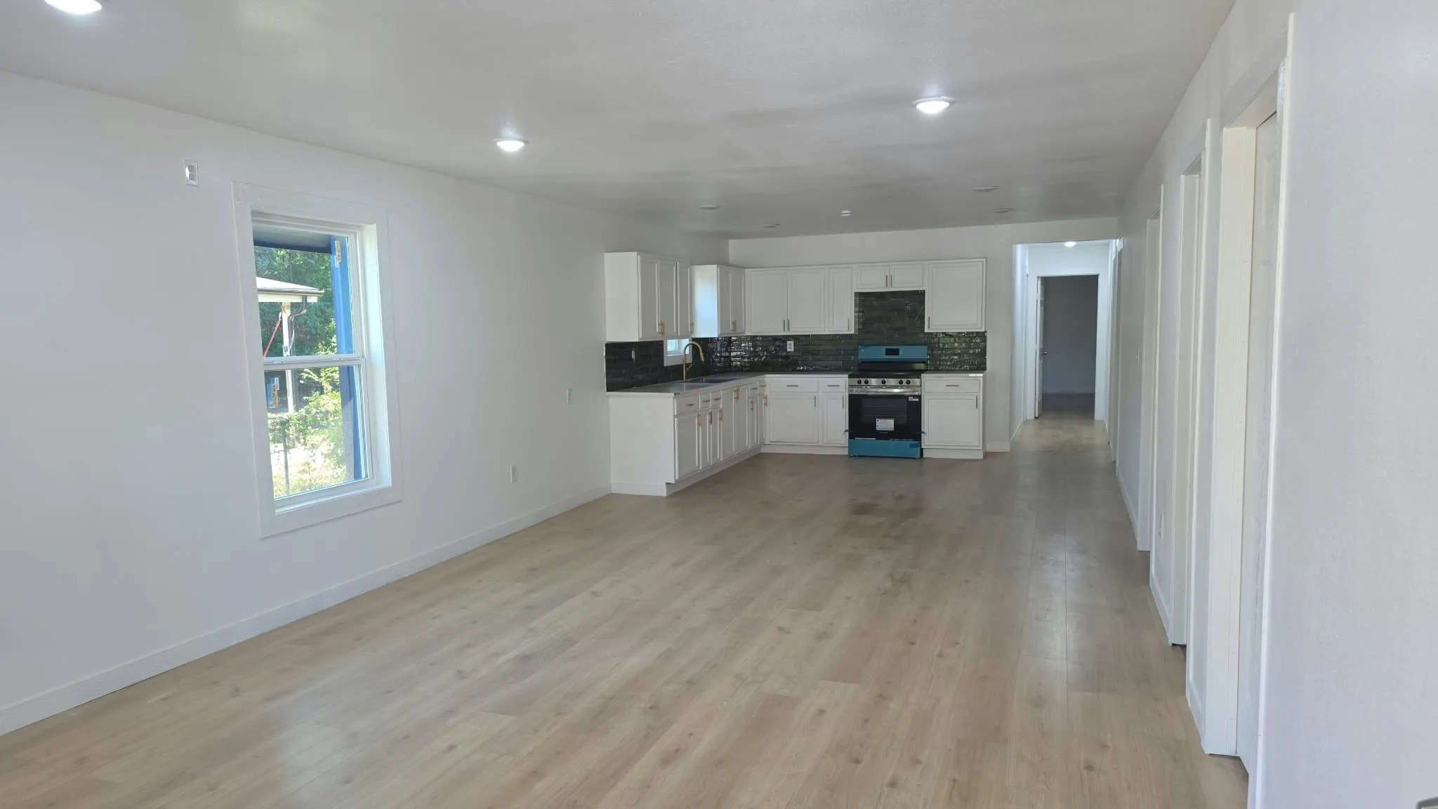 Open-concept interior featuring light-tone wood-finish flooring, recessed lighting, white cabinetry, dark tiled backsplash, and built-in appliances