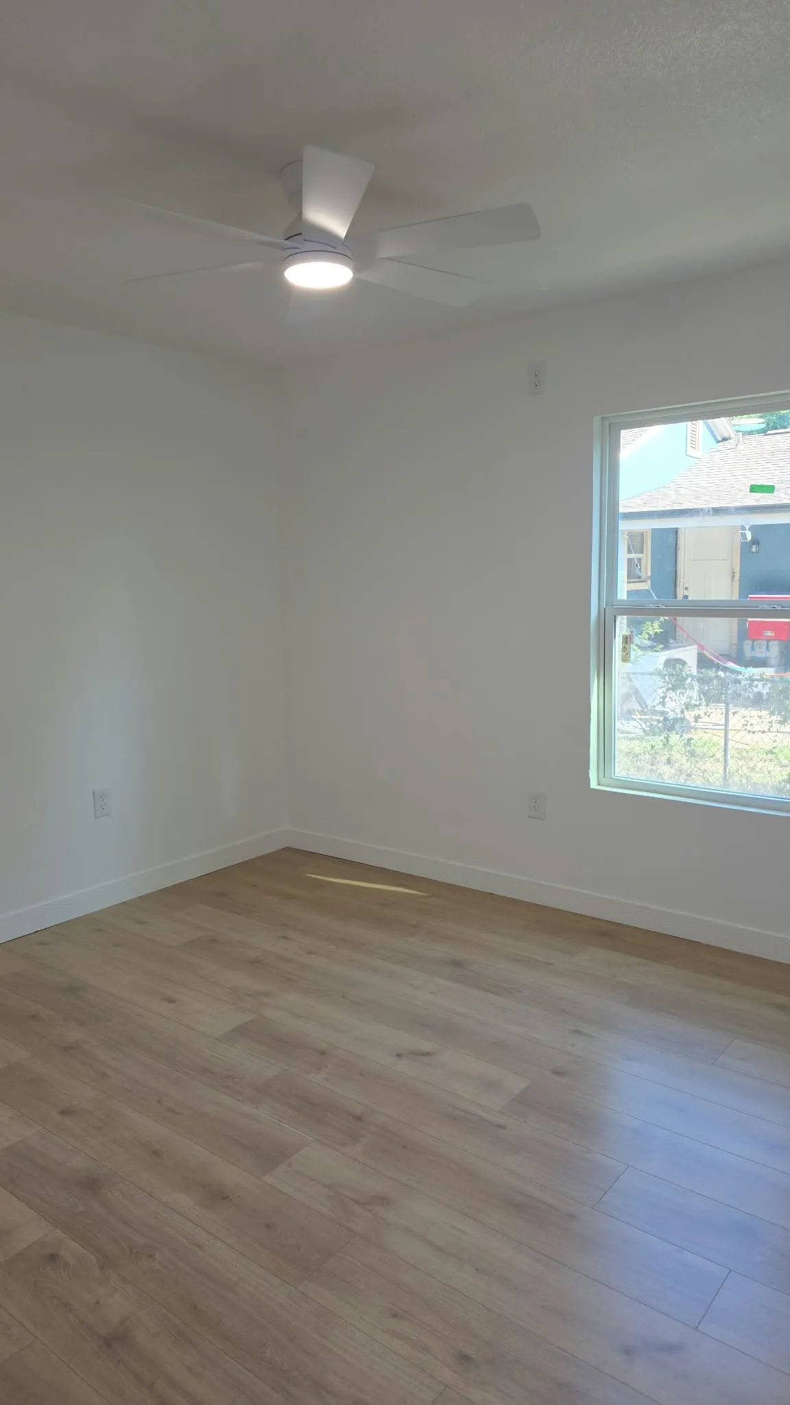 Interior room featuring wood-finish flooring, a neutral color palette, and a white ceiling fan with integrated lighting