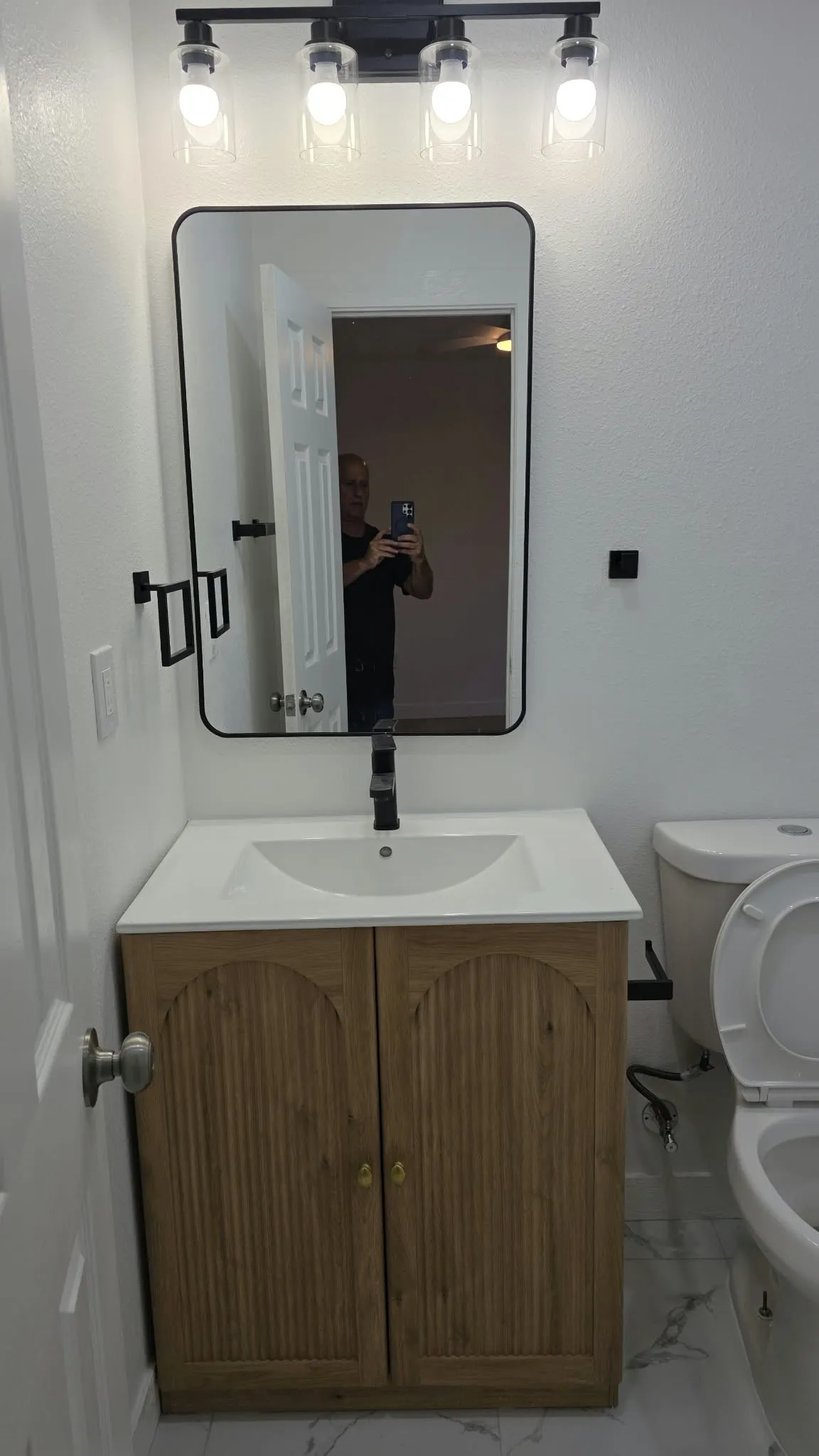 Vanity featuring a light wood-finish cabinet with arched panel doors, a white countertop, and a matte black faucet