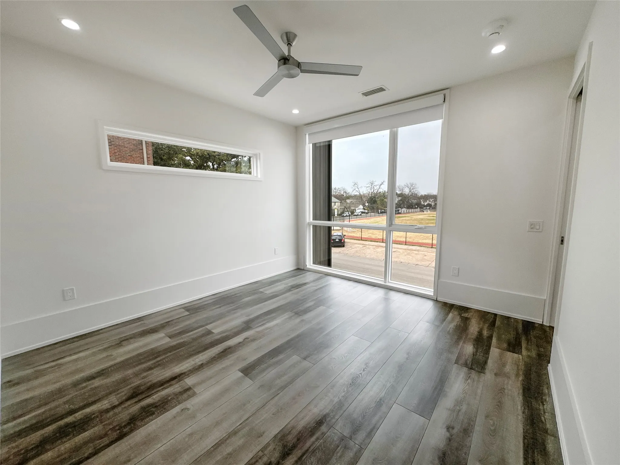 Empty room featuring dark wood-type flooring, a wealth of natural light, expansive windows, and ceiling fan