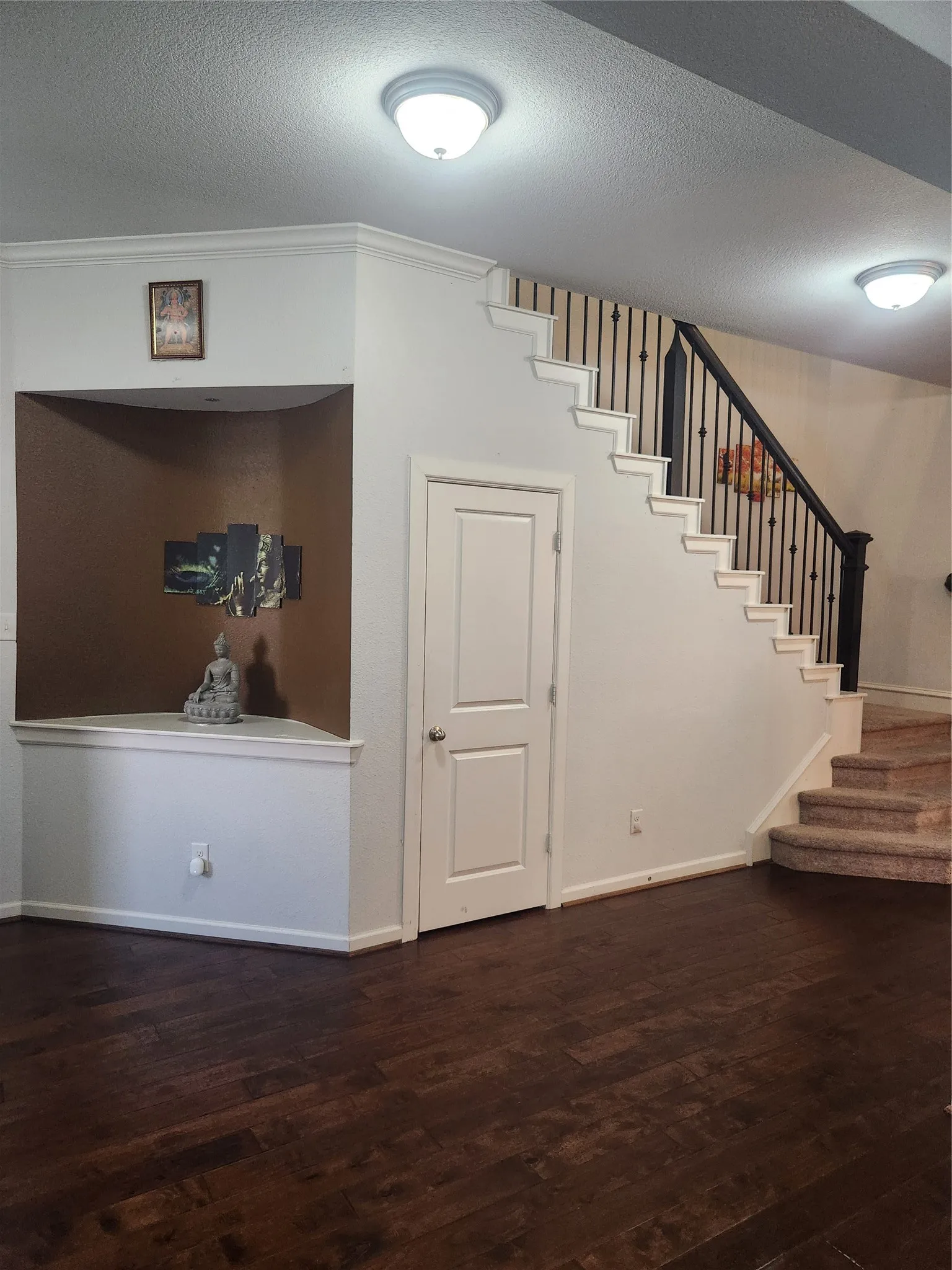 Dark wood-finish flooring, white painted walls, crown molding, built-in niche, and a staircase with dark wrought iron spindles