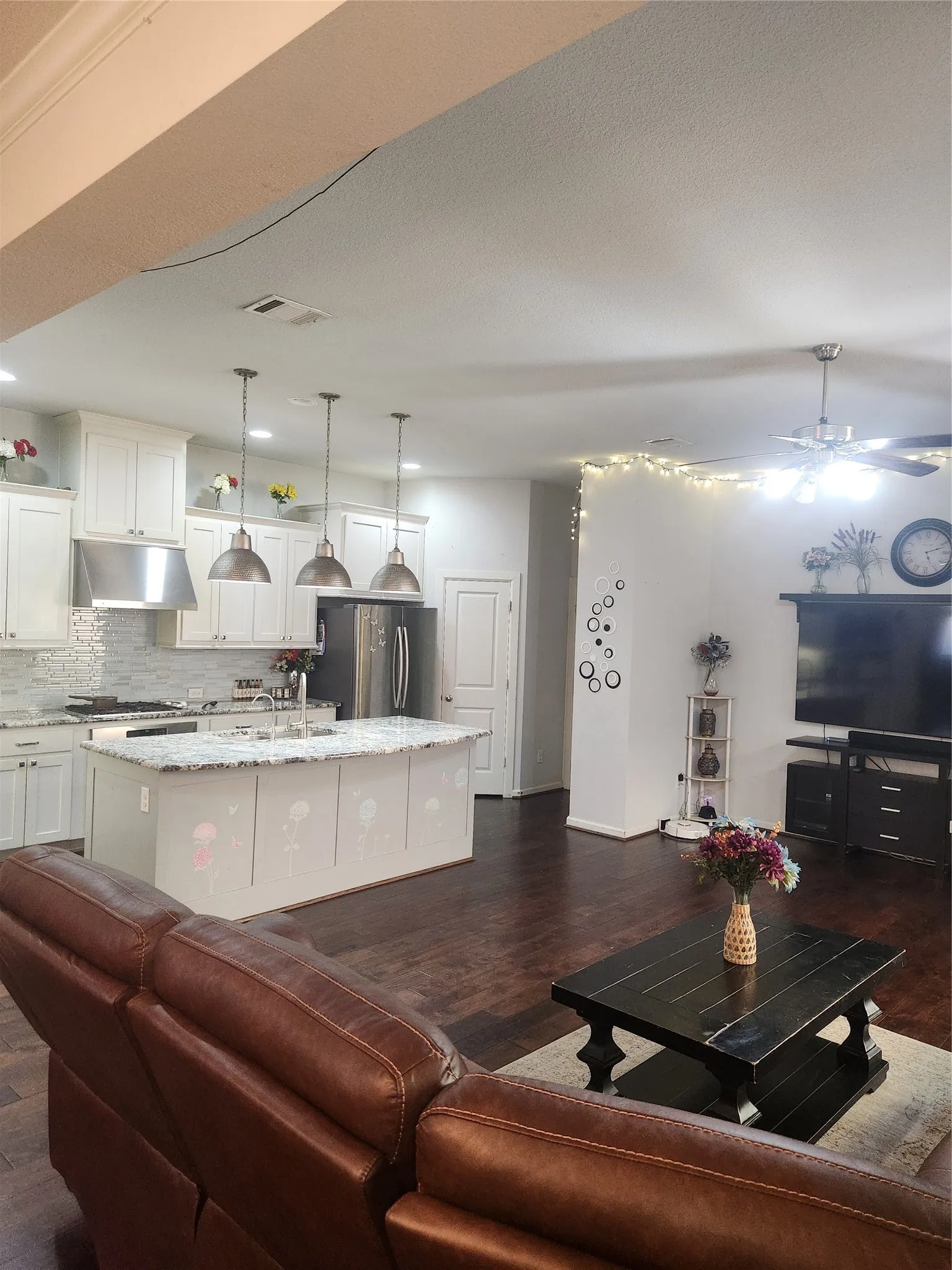 Open-concept living space with dark wood-finish flooring, white kitchen cabinetry, a kitchen island with pendant lighting, stainless steel appliances, and a ceiling fan