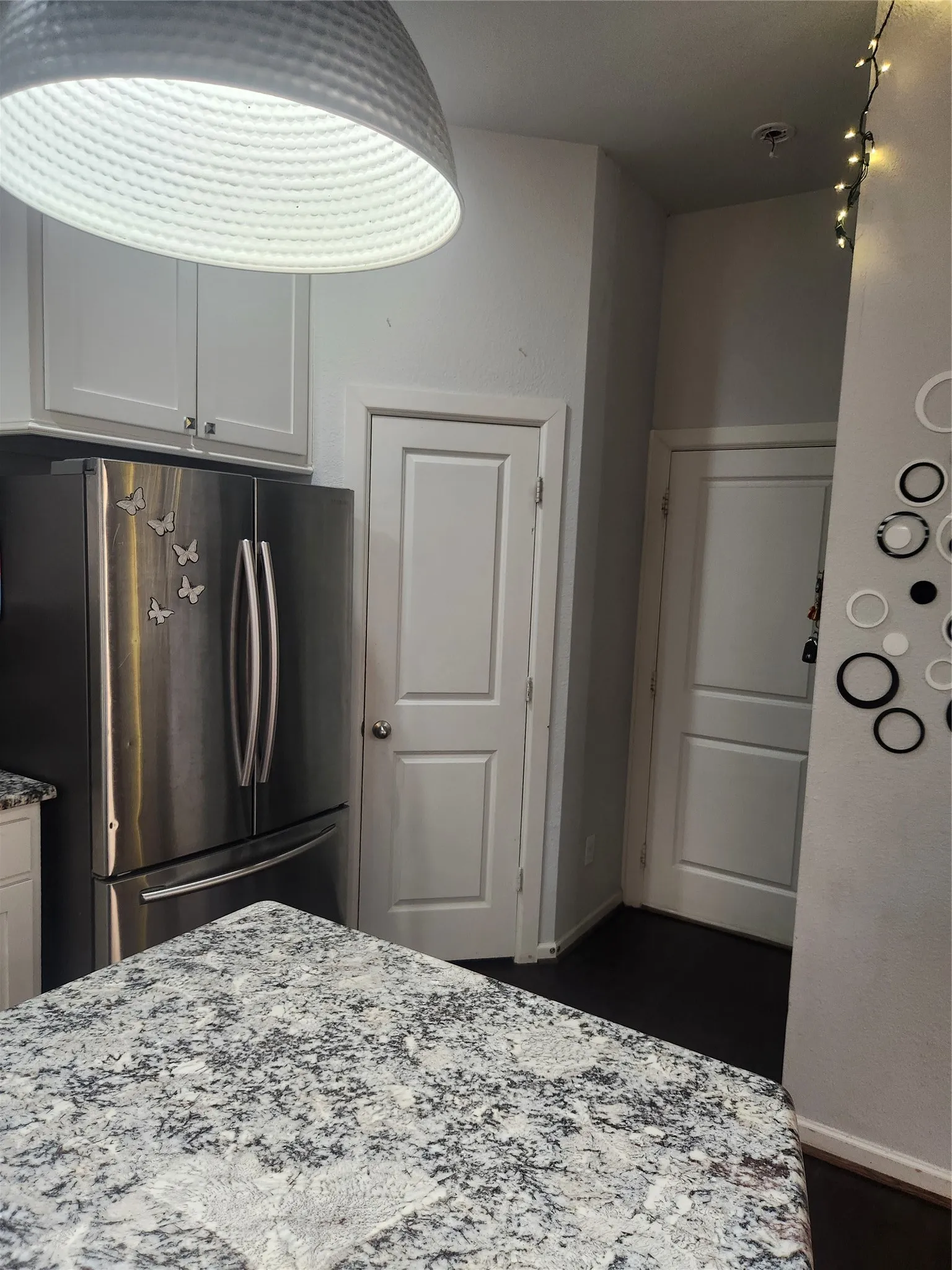 Stainless steel refrigerator, white shaker-style cabinetry, patterned countertop, dark wood-finish flooring