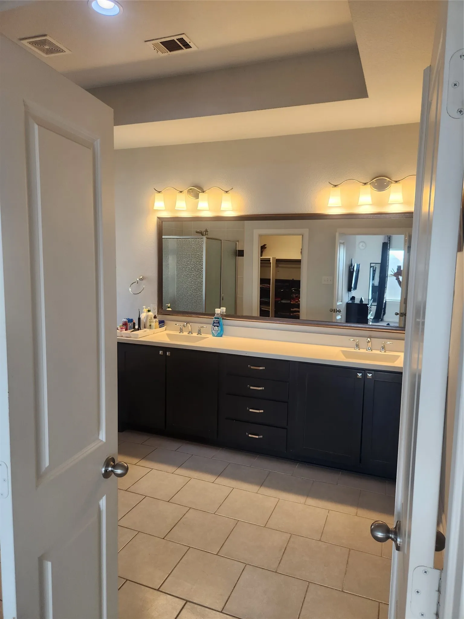 Dual vanity with undermount sinks, extensive countertop space, dark wood cabinetry, tile flooring, and recessed ceiling lighting