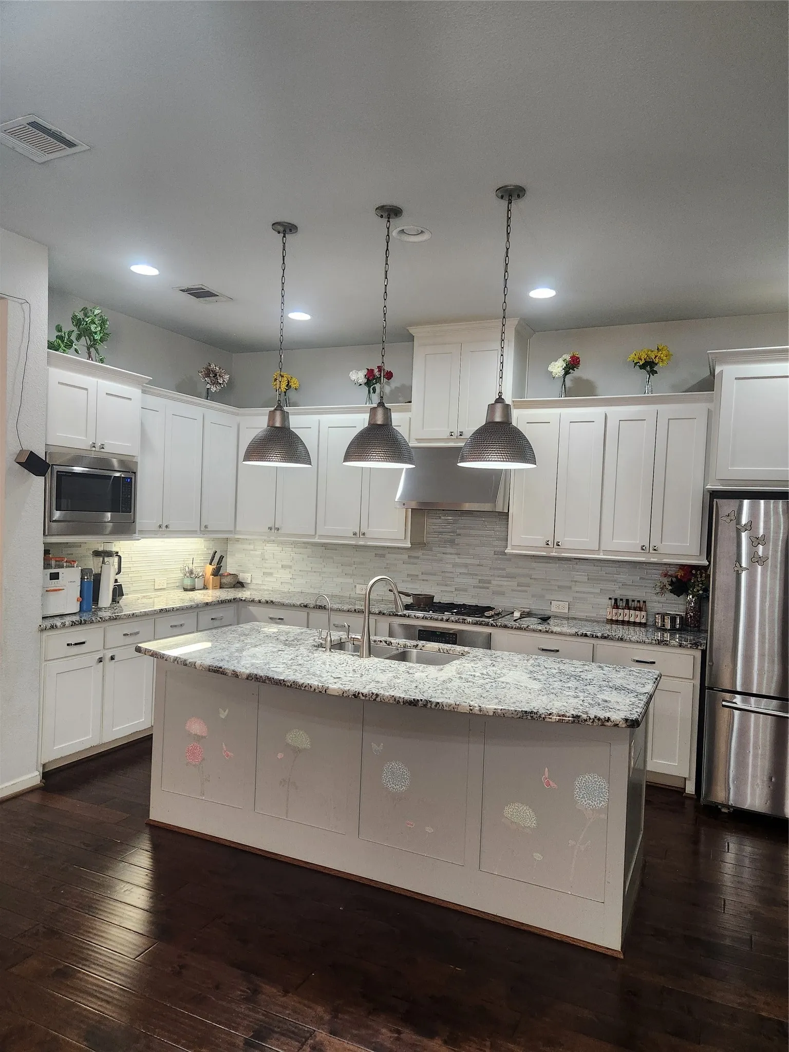 Kitchen featuring a large island with a stone countertop, dark wood-finish flooring, white cabinetry, stainless steel appliances, and a tile backsplash