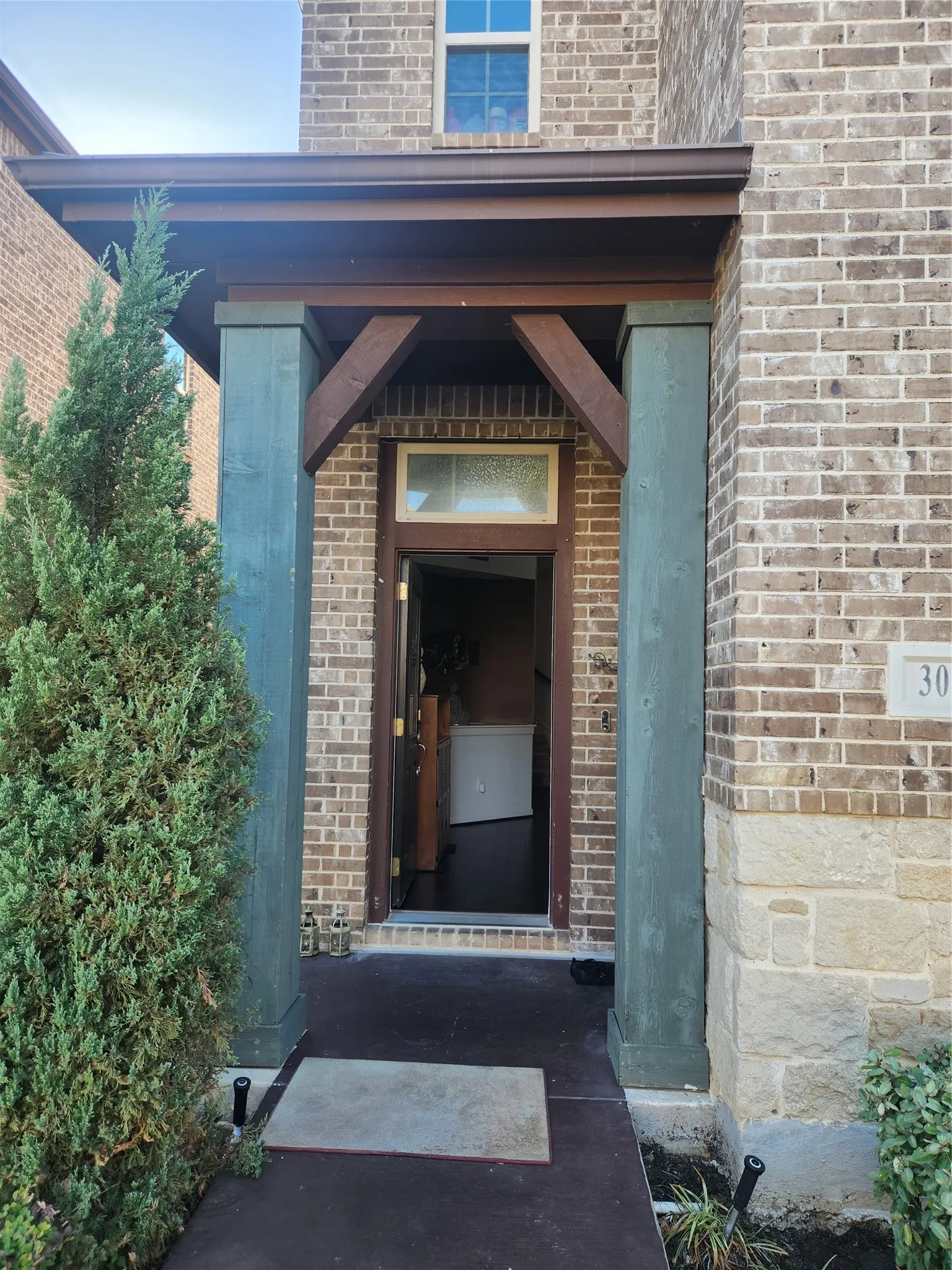 Brick exterior with stone accents, covered entryway with wood-finish beams, and transom window above the door