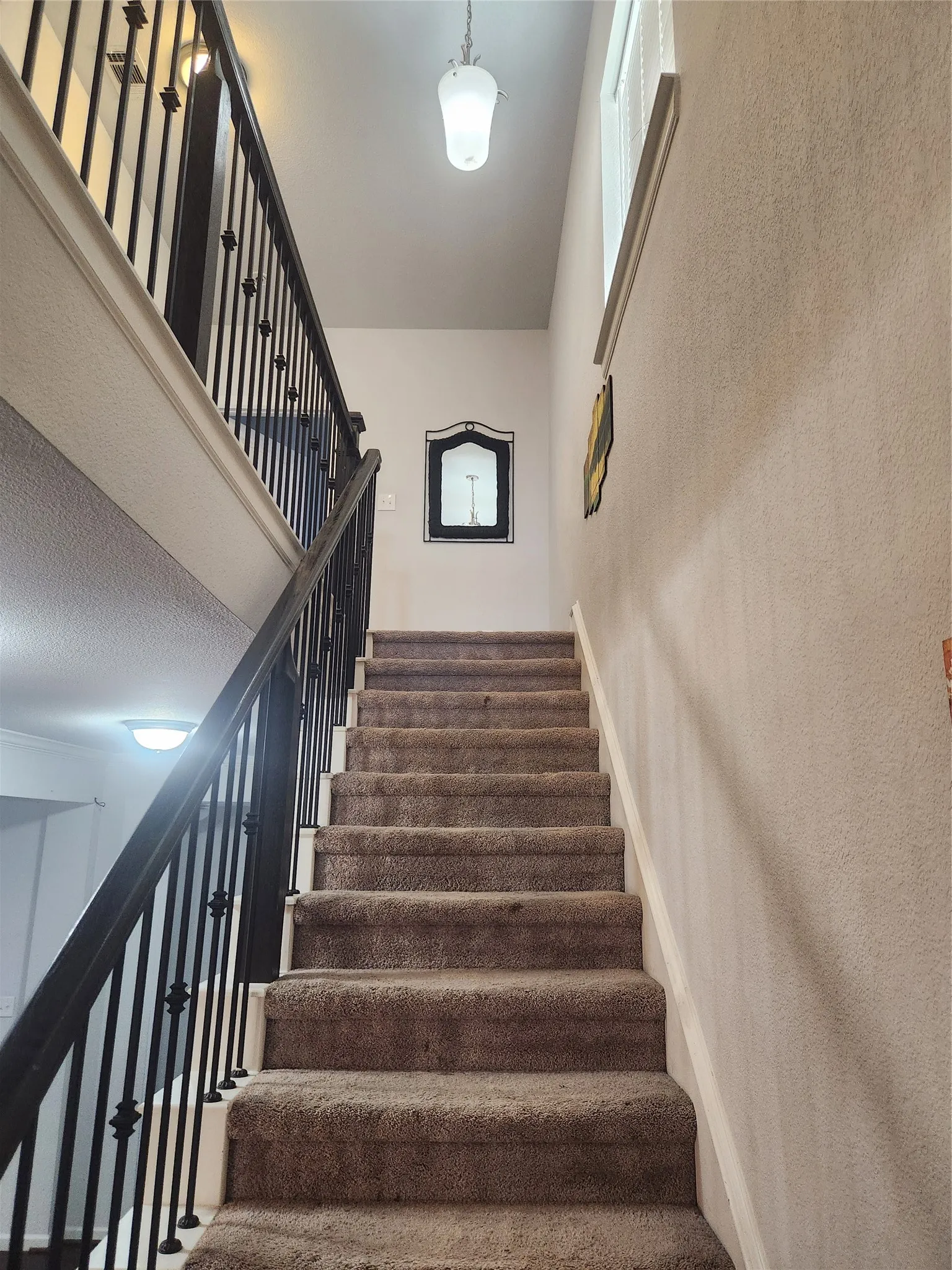 Carpeted staircase with wrought iron balusters and a pendant light fixture