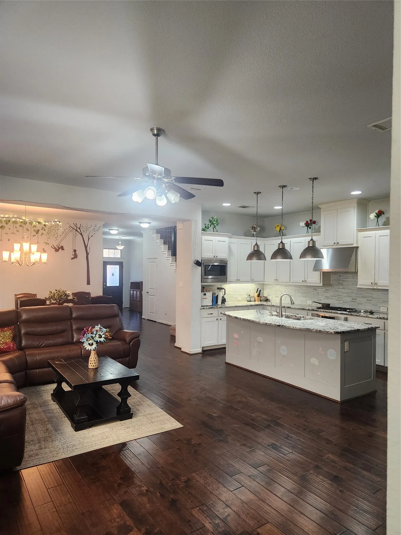 Expansive wood-finish flooring throughout, kitchen with white cabinetry, large center island with stone countertop, stainless steel appliances, and pendant lighting