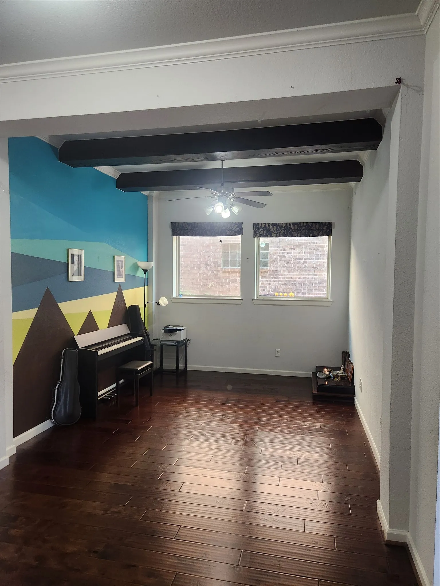 Wood-finish flooring, exposed ceiling beams, white crown molding, ceiling fan with integrated lighting, and multiple windows